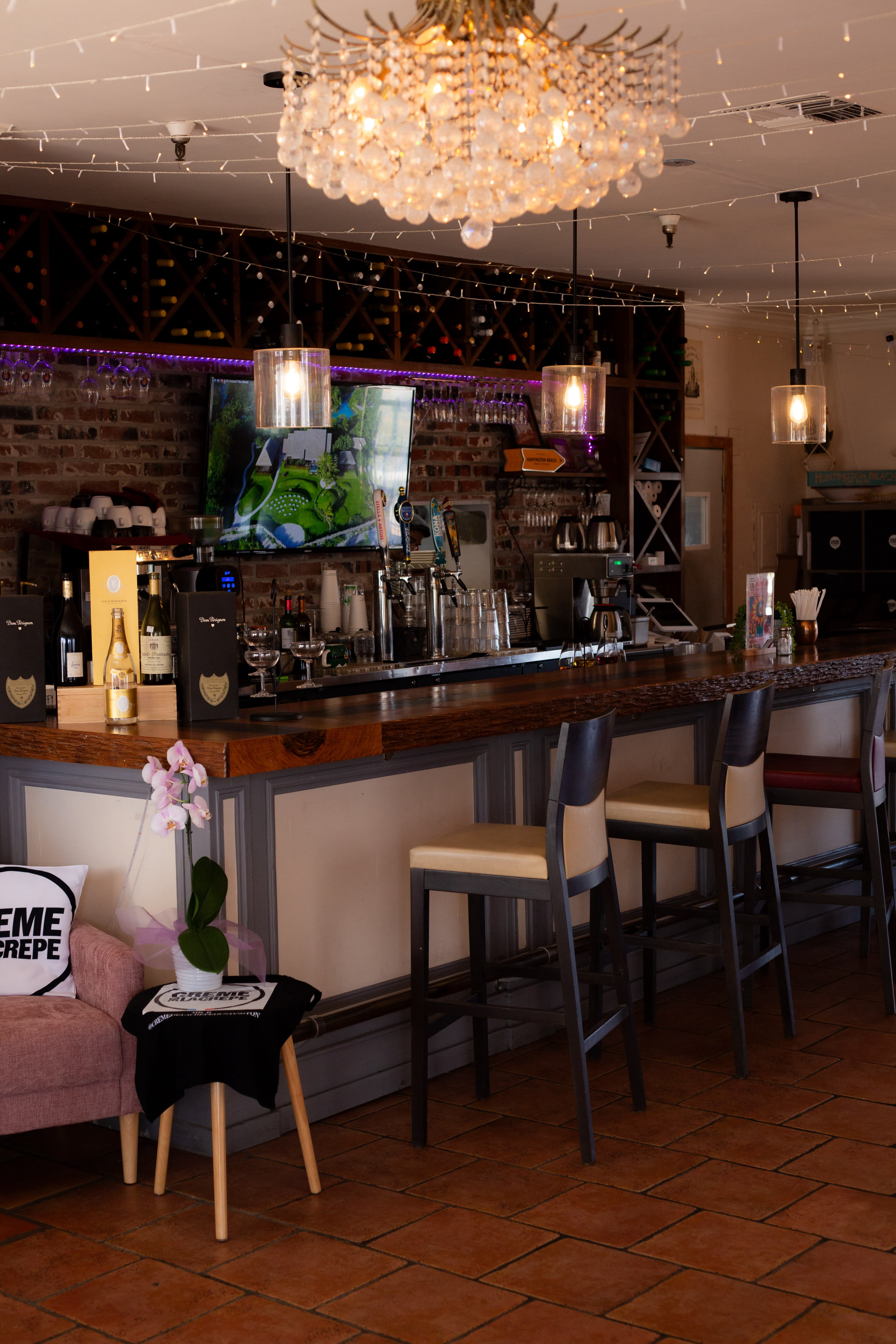 The image shows an inviting bar area with a wooden counter, high stools, a television screen, and decorative lighting elements.