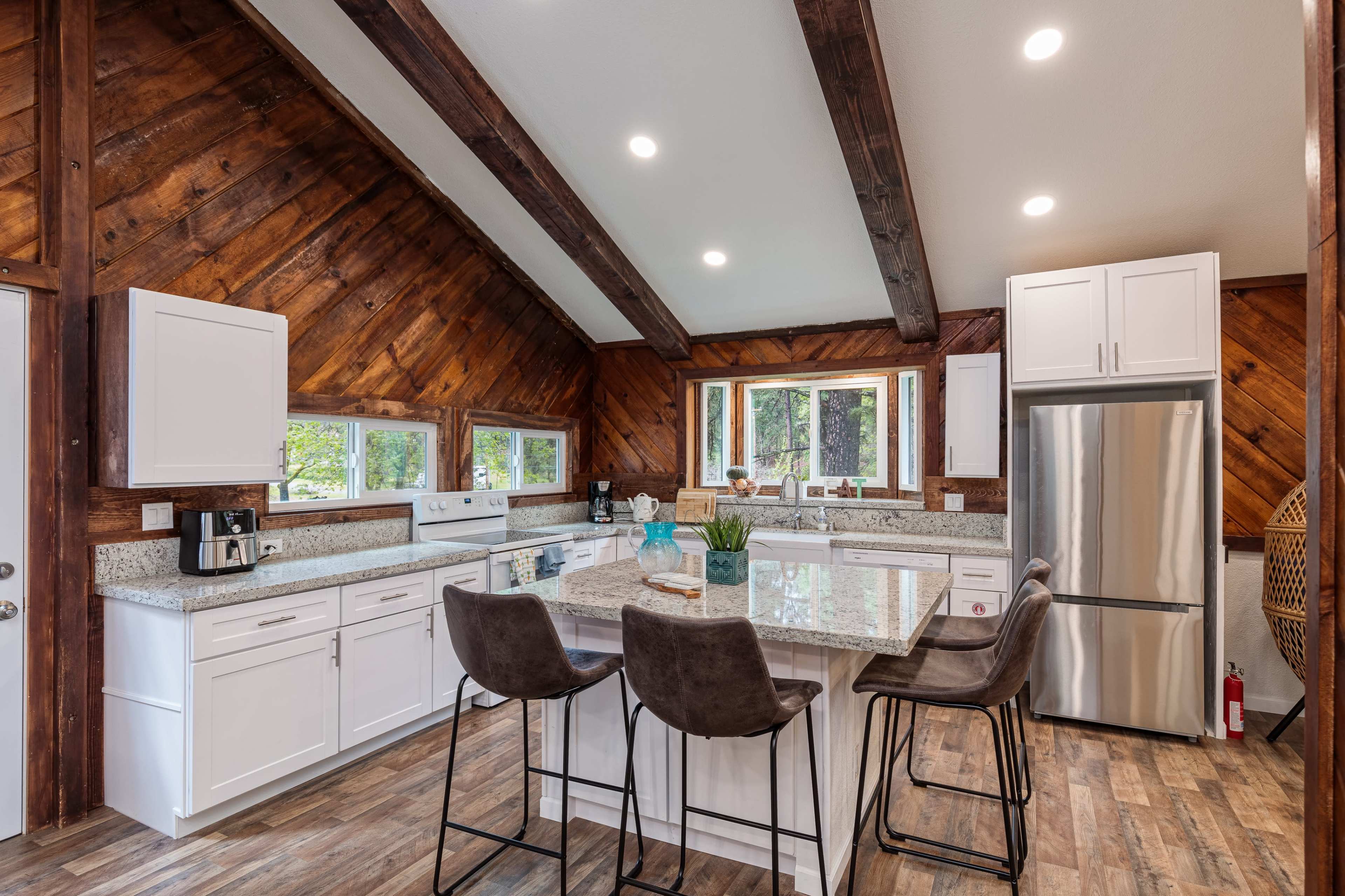 A modern kitchen with a large island, white cabinetry, stainless steel appliances, and wood-paneled vaulted ceilings.