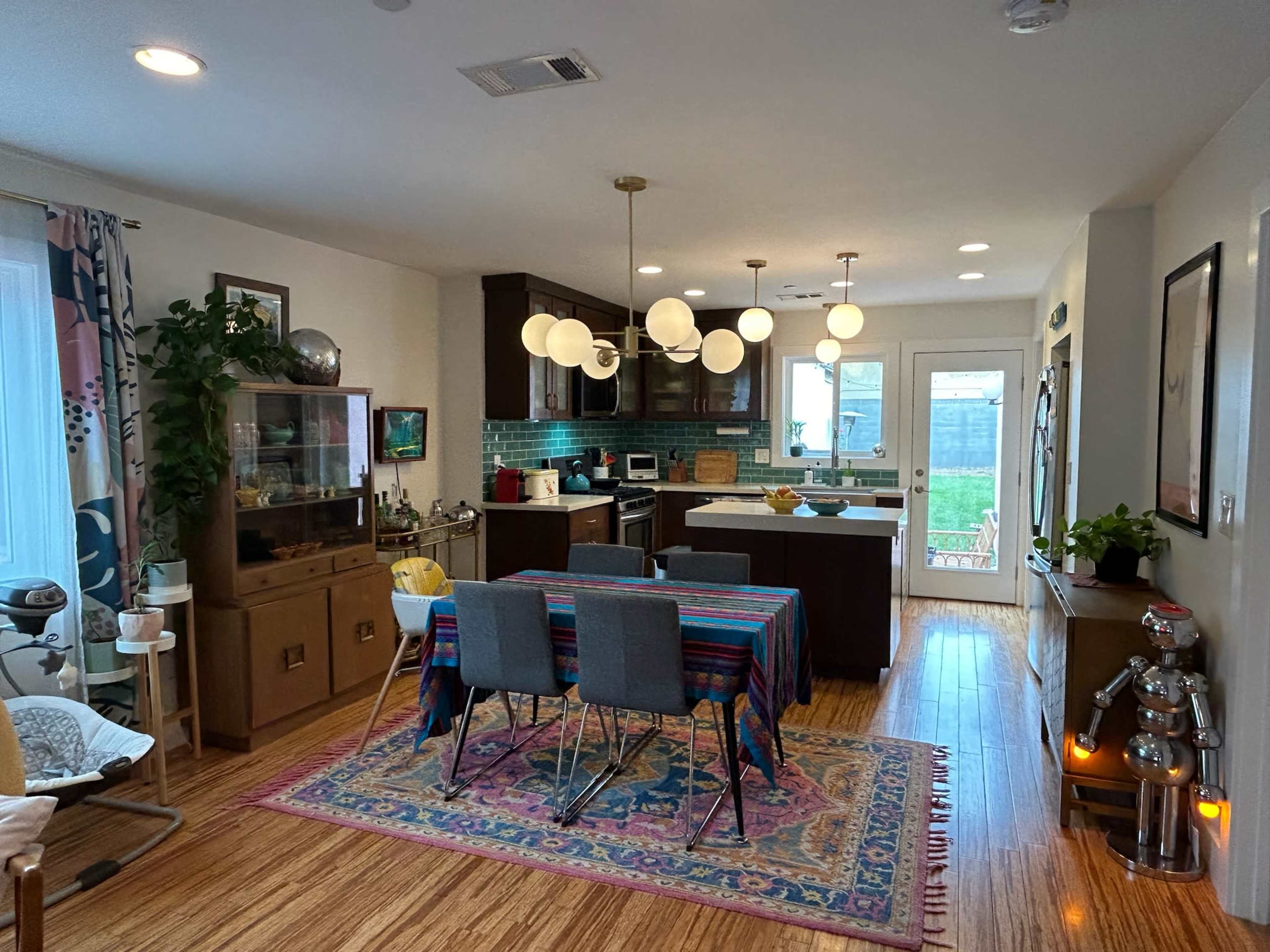 A modern kitchen and dining area featuring a colorful tablecloth, a wooden dining table with chairs, and large pendant lights above.