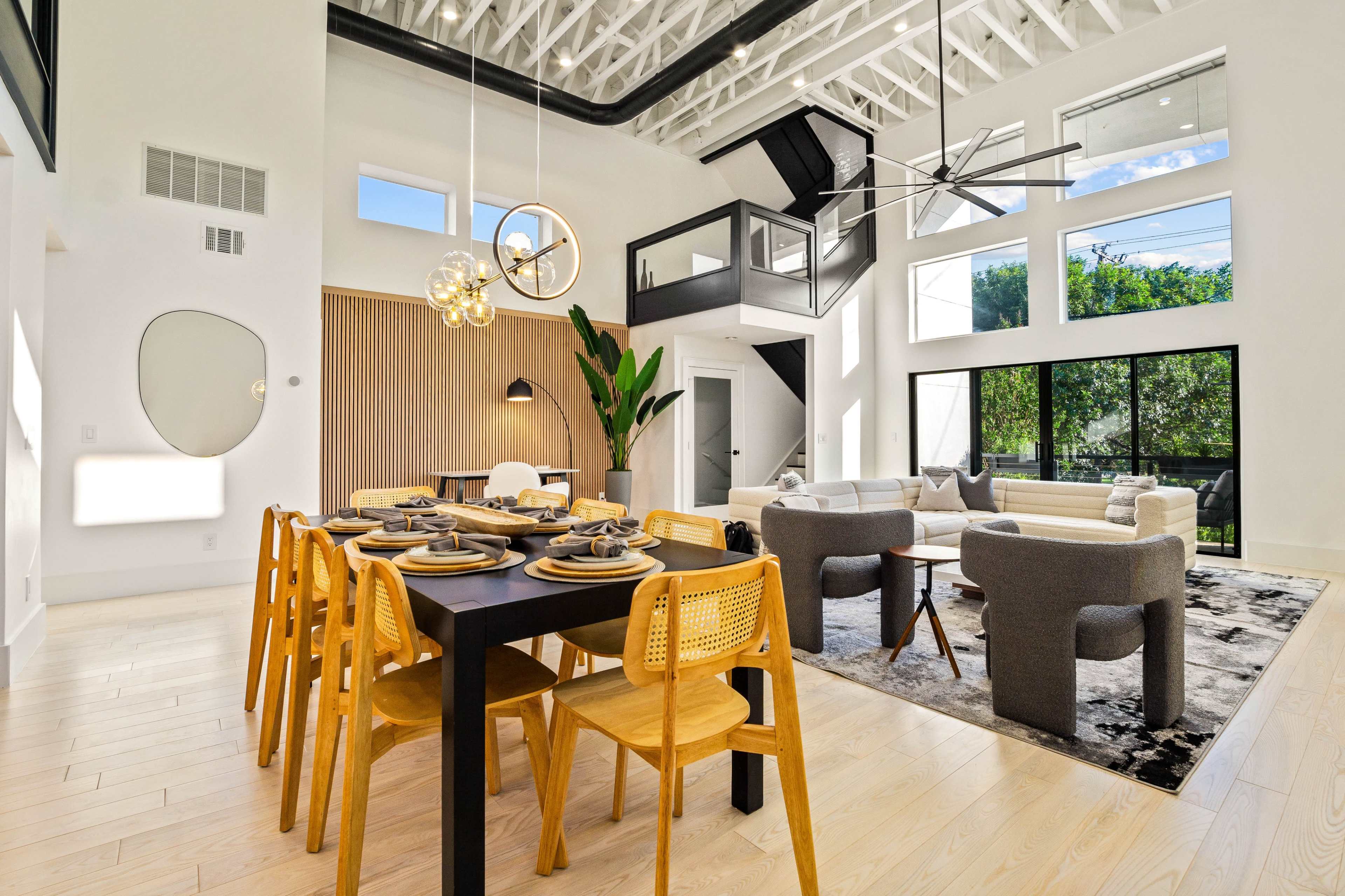 A modern open-concept living and dining area with high ceilings, large windows, and contemporary furnishings.