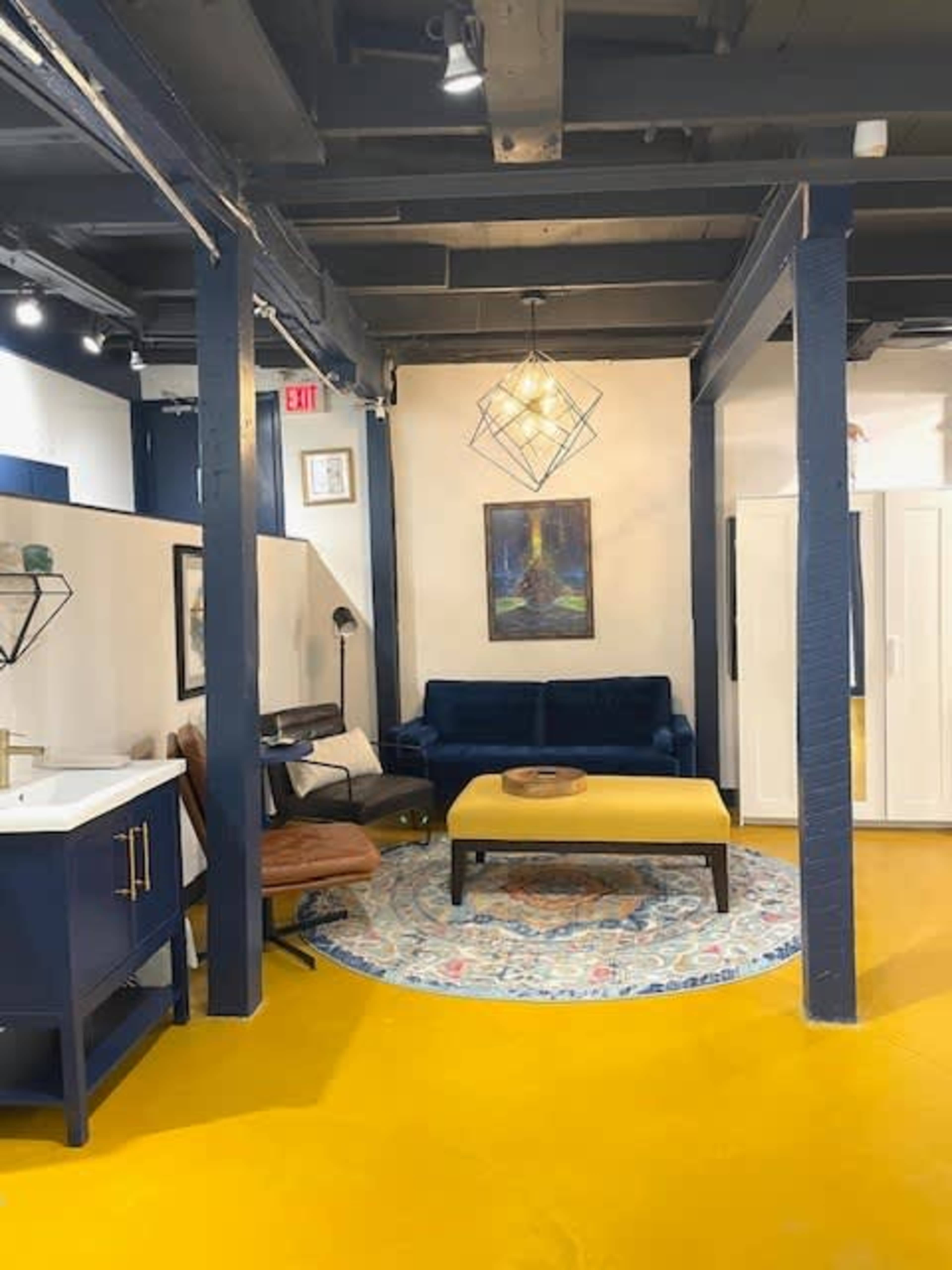 The image shows a modern living space with a yellow floor, a blue sofa, a brown chair, a round coffee table, and art on the walls.
