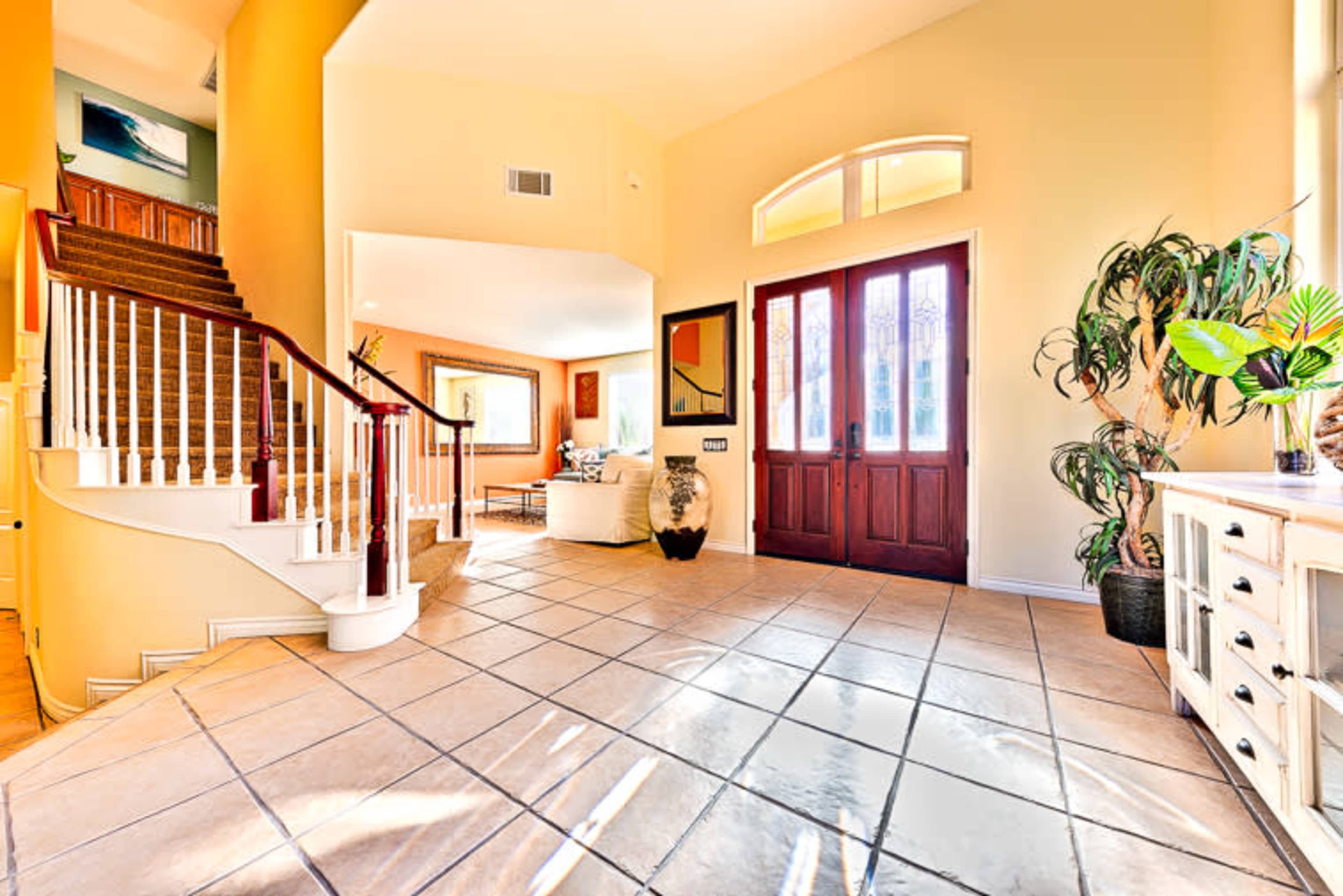 A spacious entryway with a curved staircase, tile flooring, and large double doors opening into a well-lit living area.