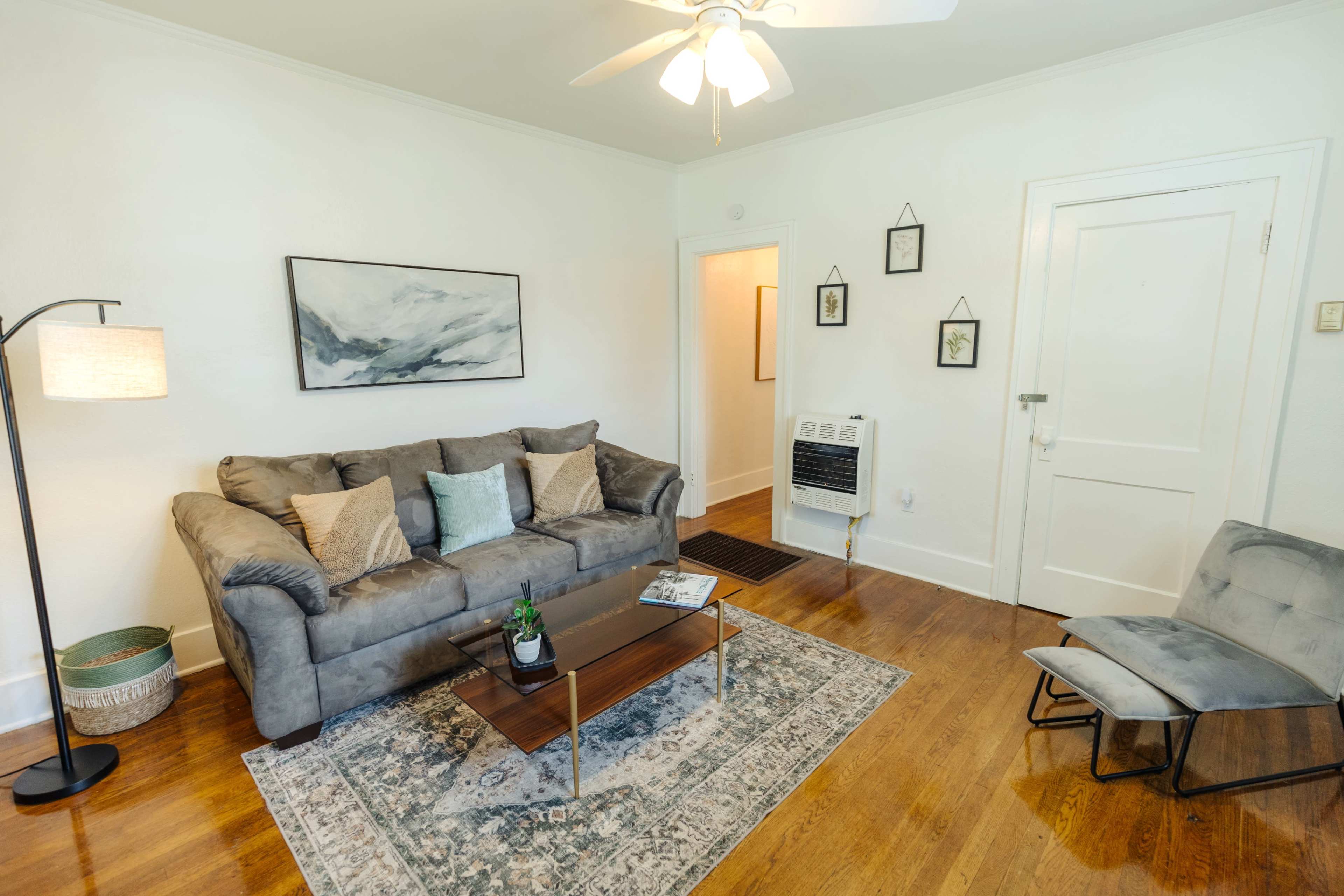 A living room with a grey couch, a coffee table, and a light-colored wall with framed artwork.