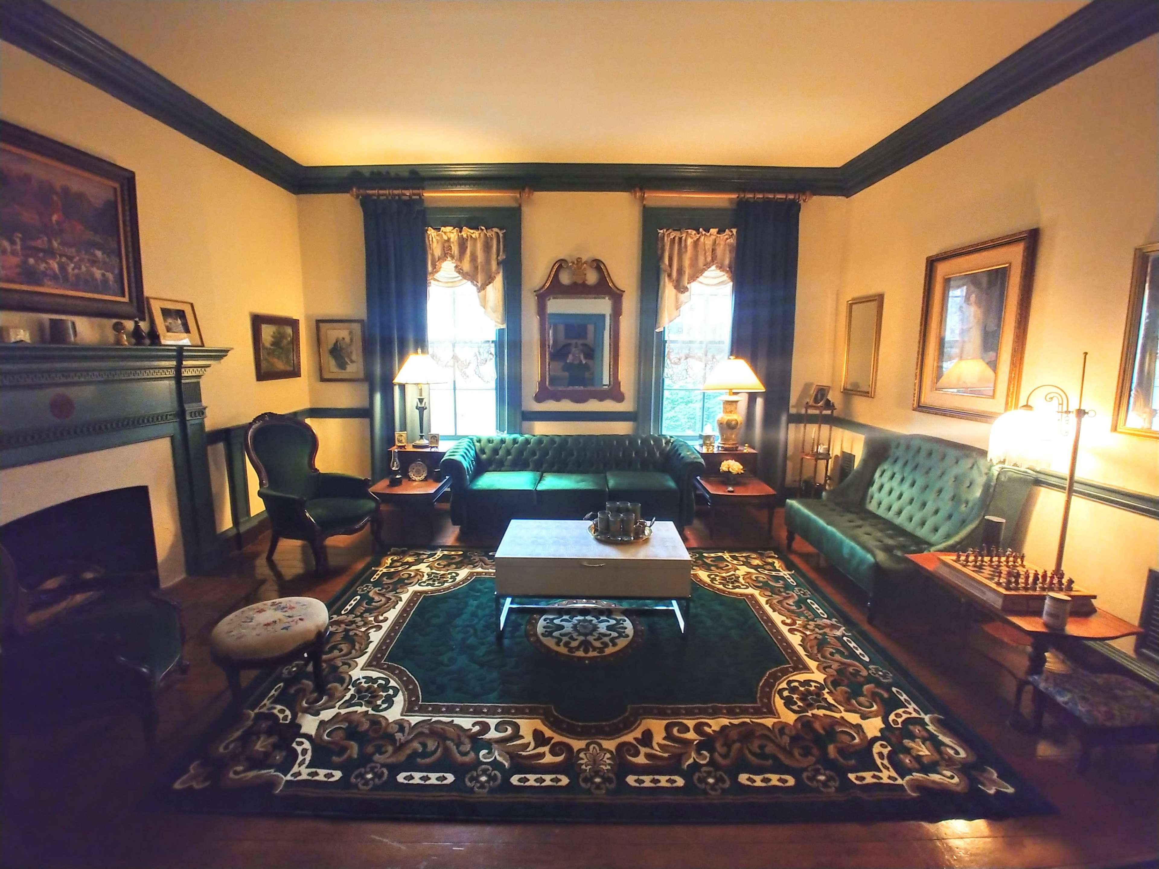 The room features green upholstered furniture, a decorative rug, a fireplace, and framed artworks on the walls.