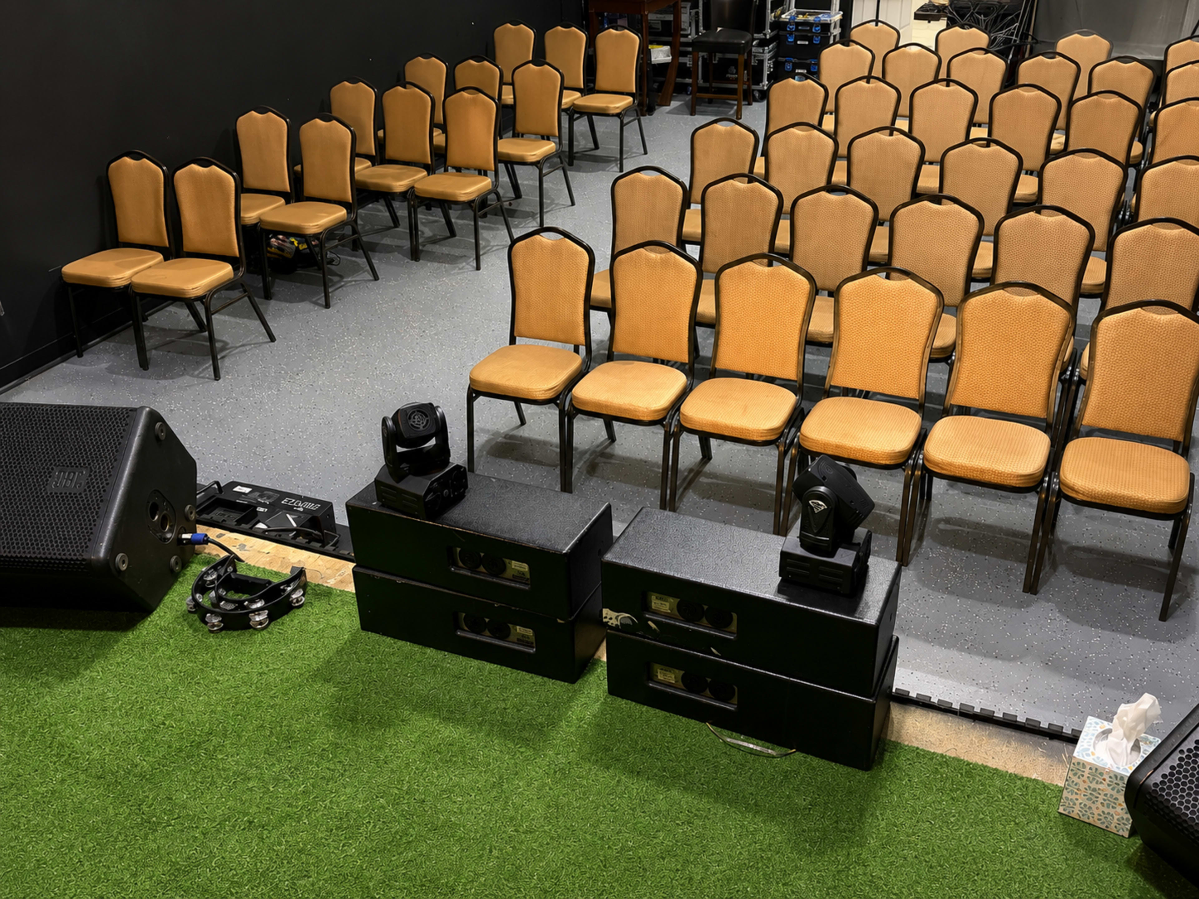 The image shows a setup for an event with neatly arranged rows of empty orange chairs facing a sound system and stage area.