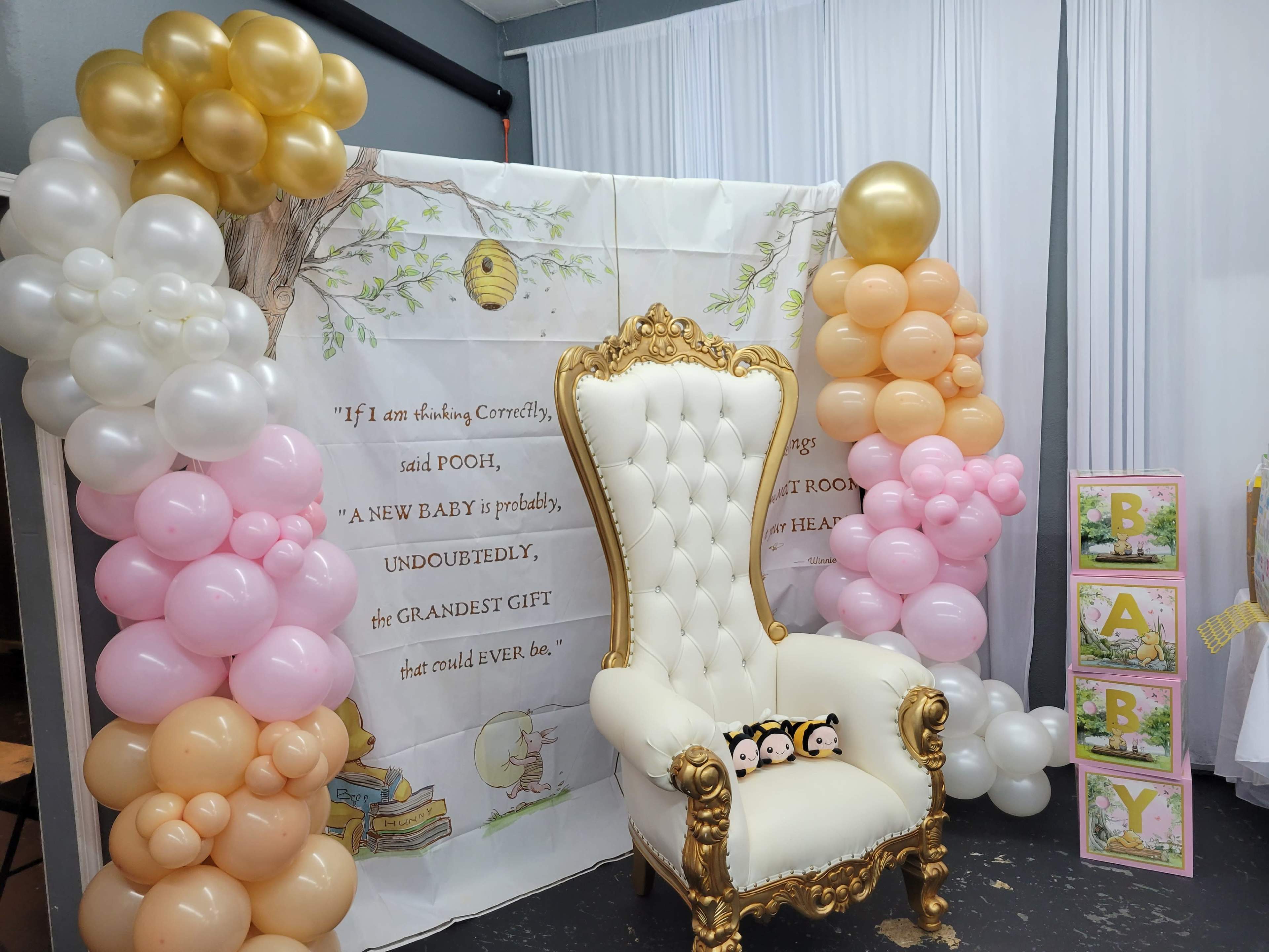 A decorated backdrop with a throne chair surrounded by pastel balloons, featuring a quote about welcoming a new baby.