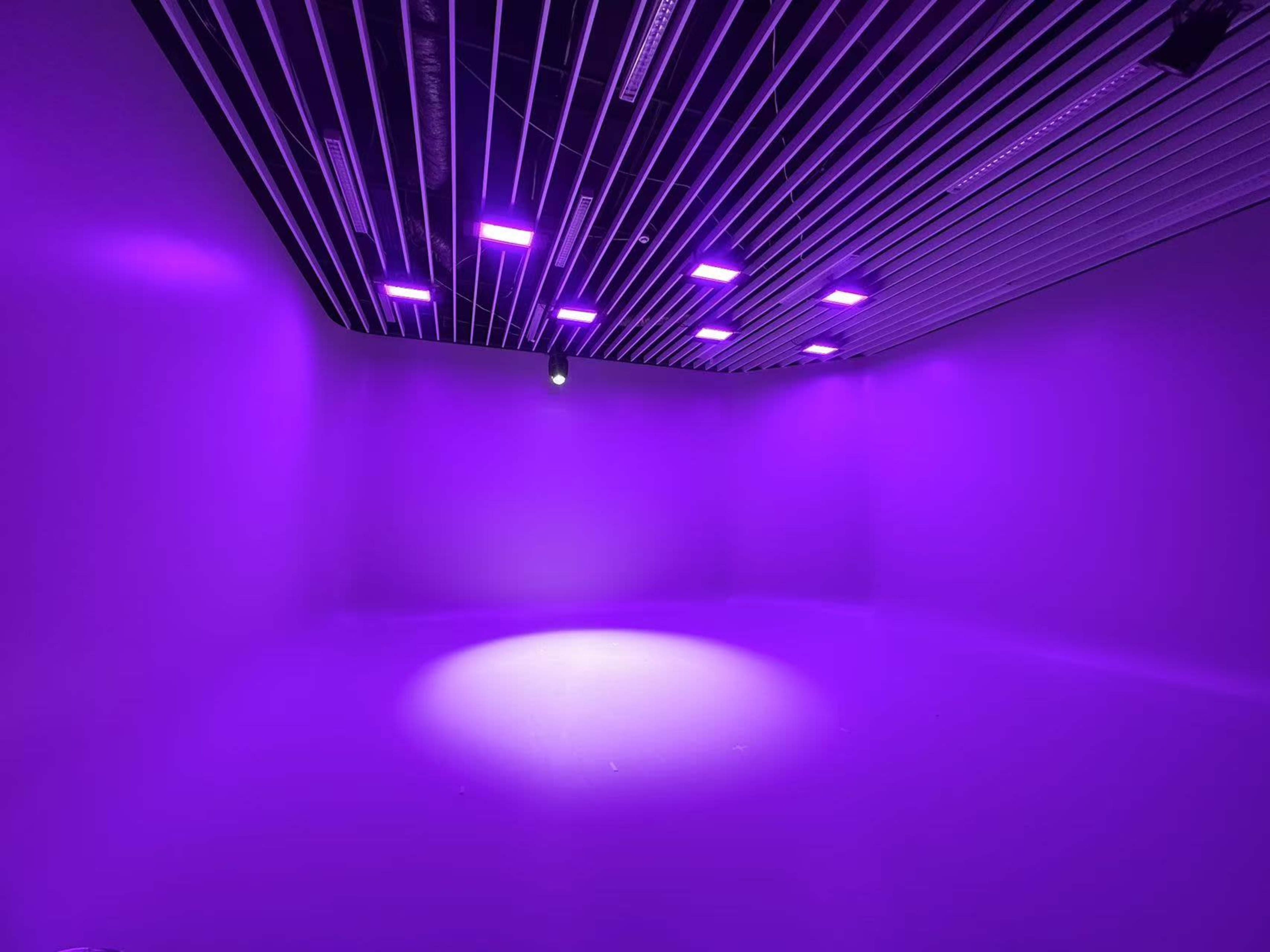 A minimalist room is illuminated with purple lights casting a focused beam on the floor.