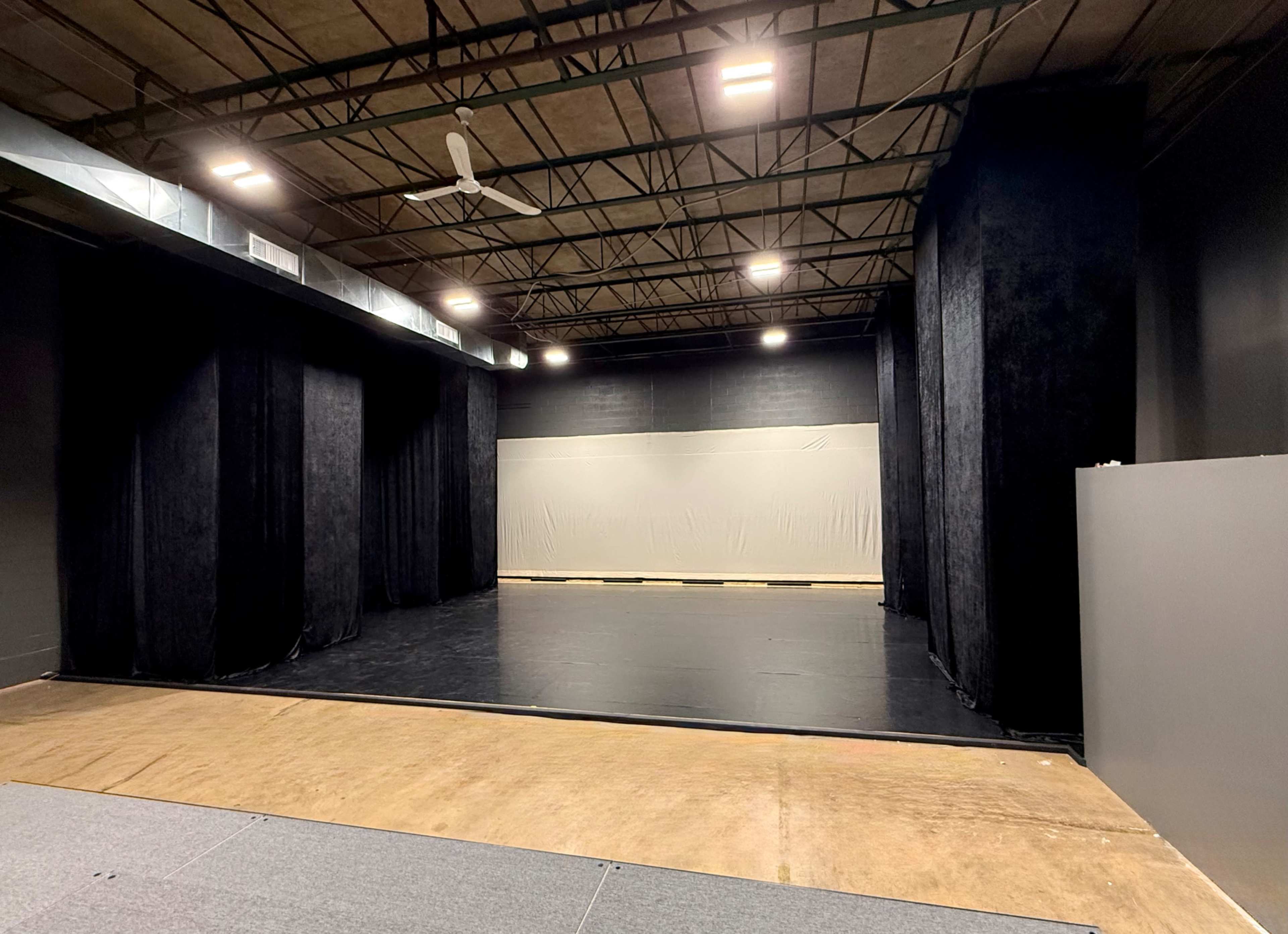 The image shows an empty stage area with black curtains and a large gray backdrop in a spacious room.