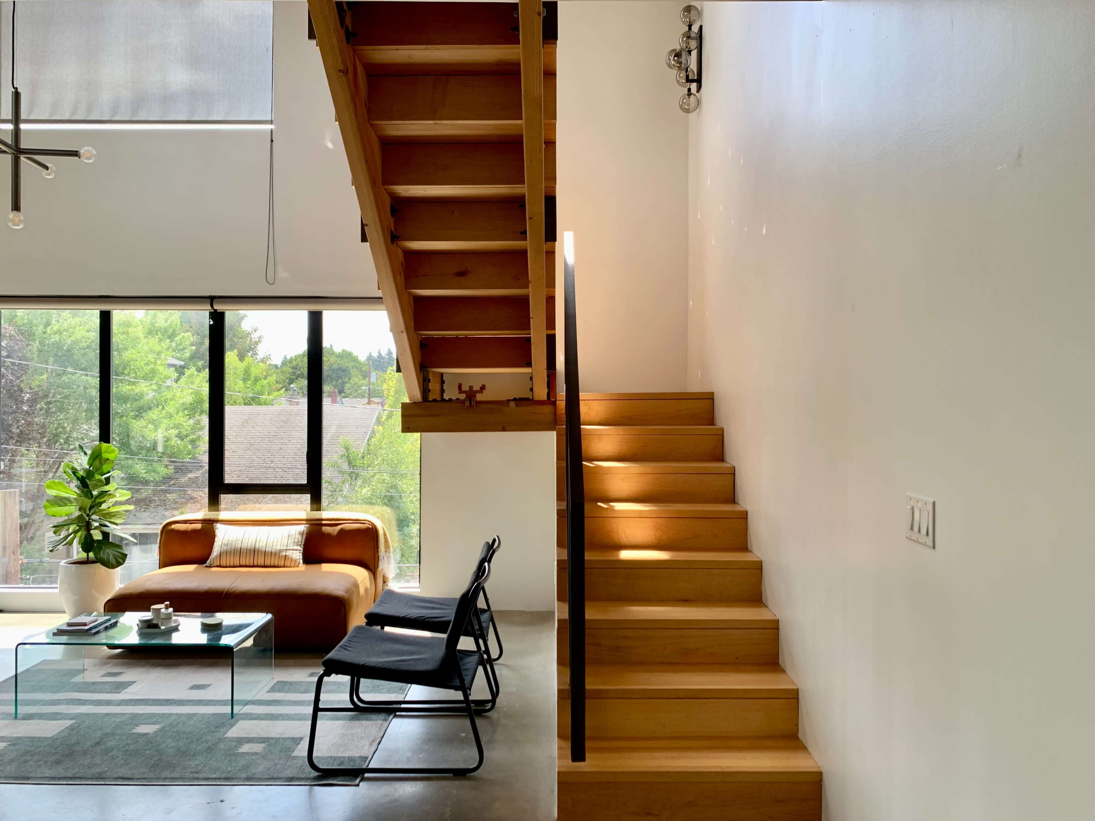 A modern interior features a wooden staircase leading to an upper level, next to a seating area with a brown sofa and a glass coffee table.
