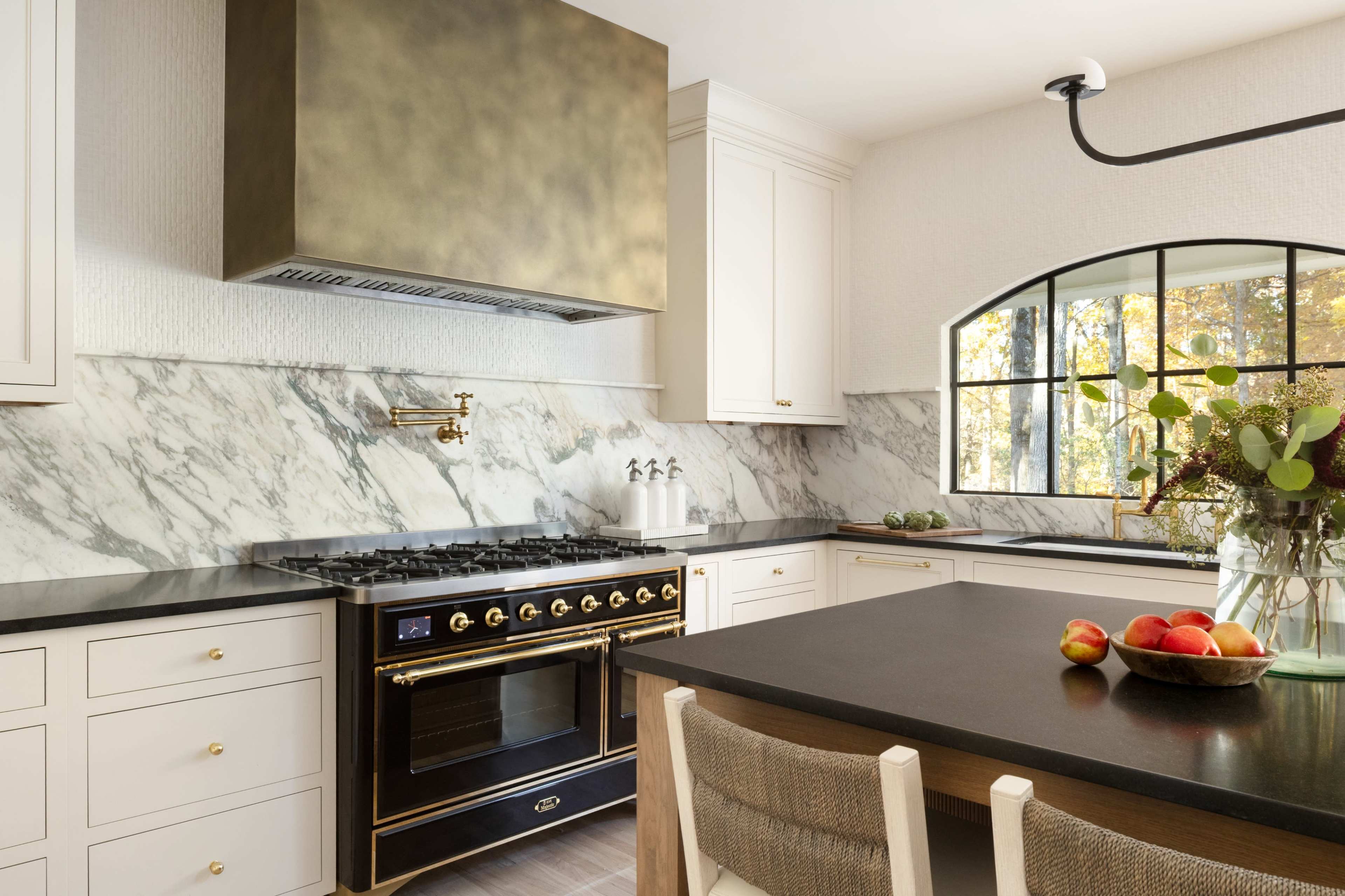 The kitchen features a black and gold stove, marble backsplash, and a large window with a view.
