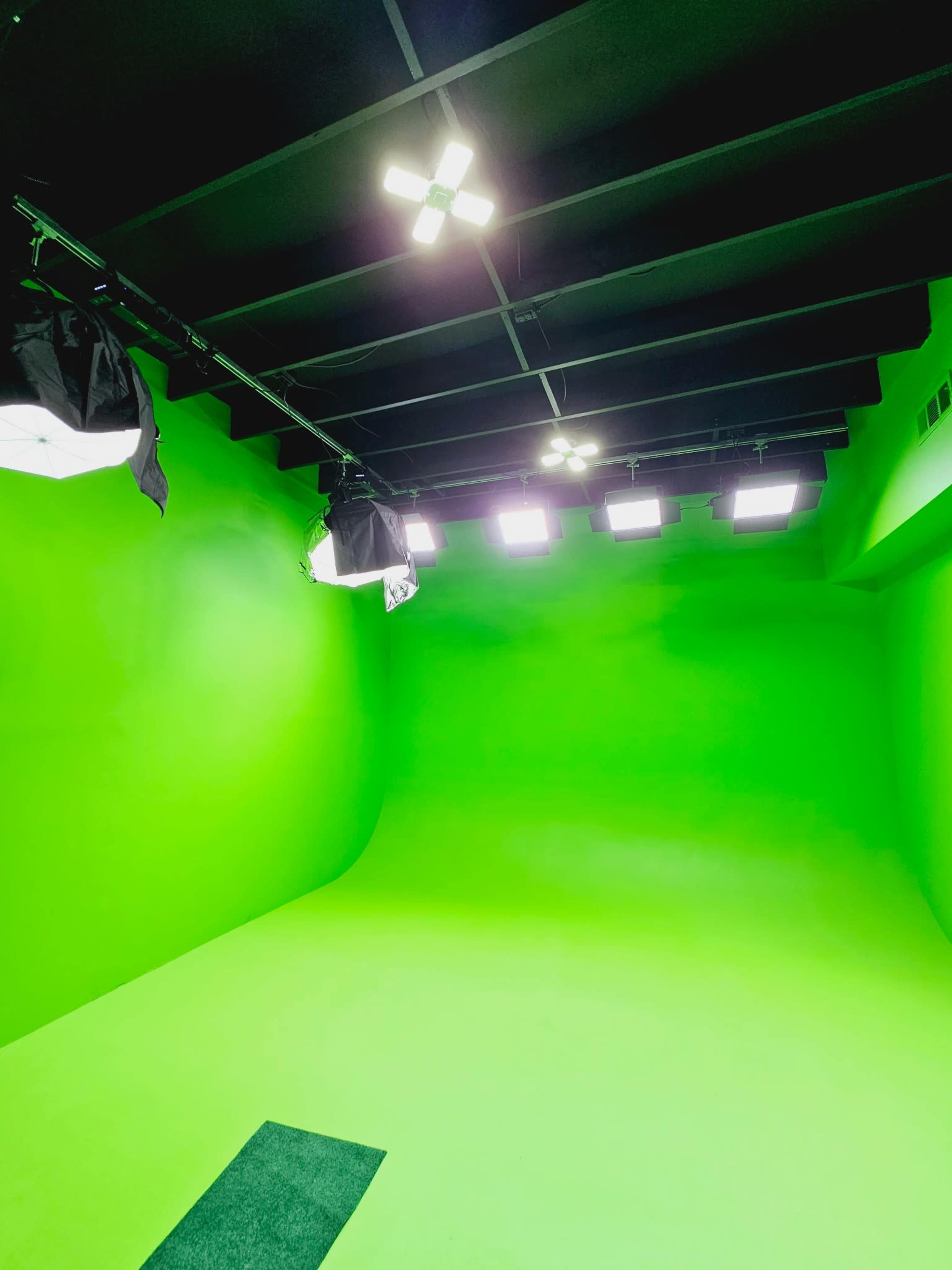A green screen room with bright lighting and black softbox lighting equipment mounted on the ceiling.