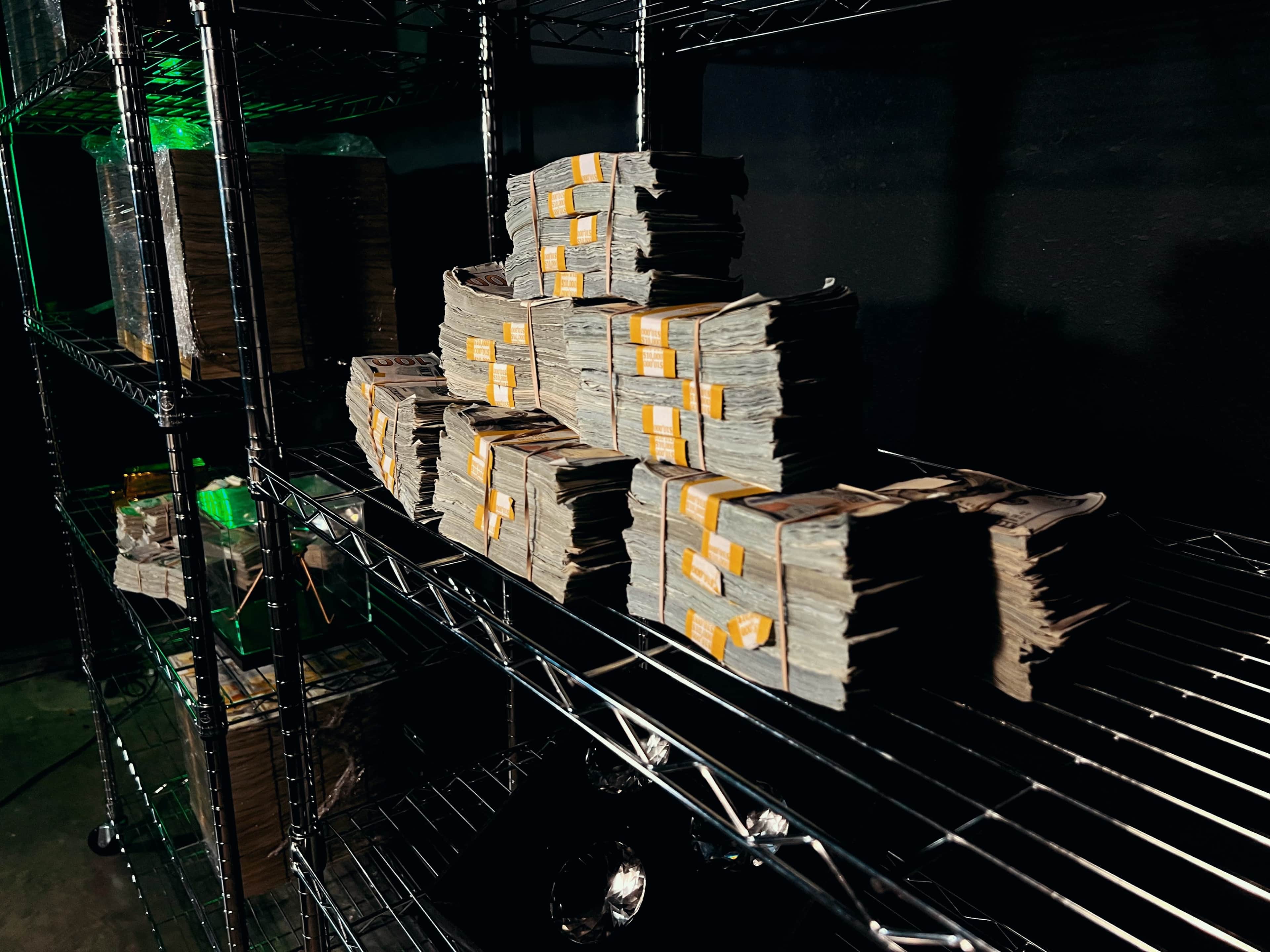 Stacks of cash are neatly arranged on wire shelving in a dimly lit room.