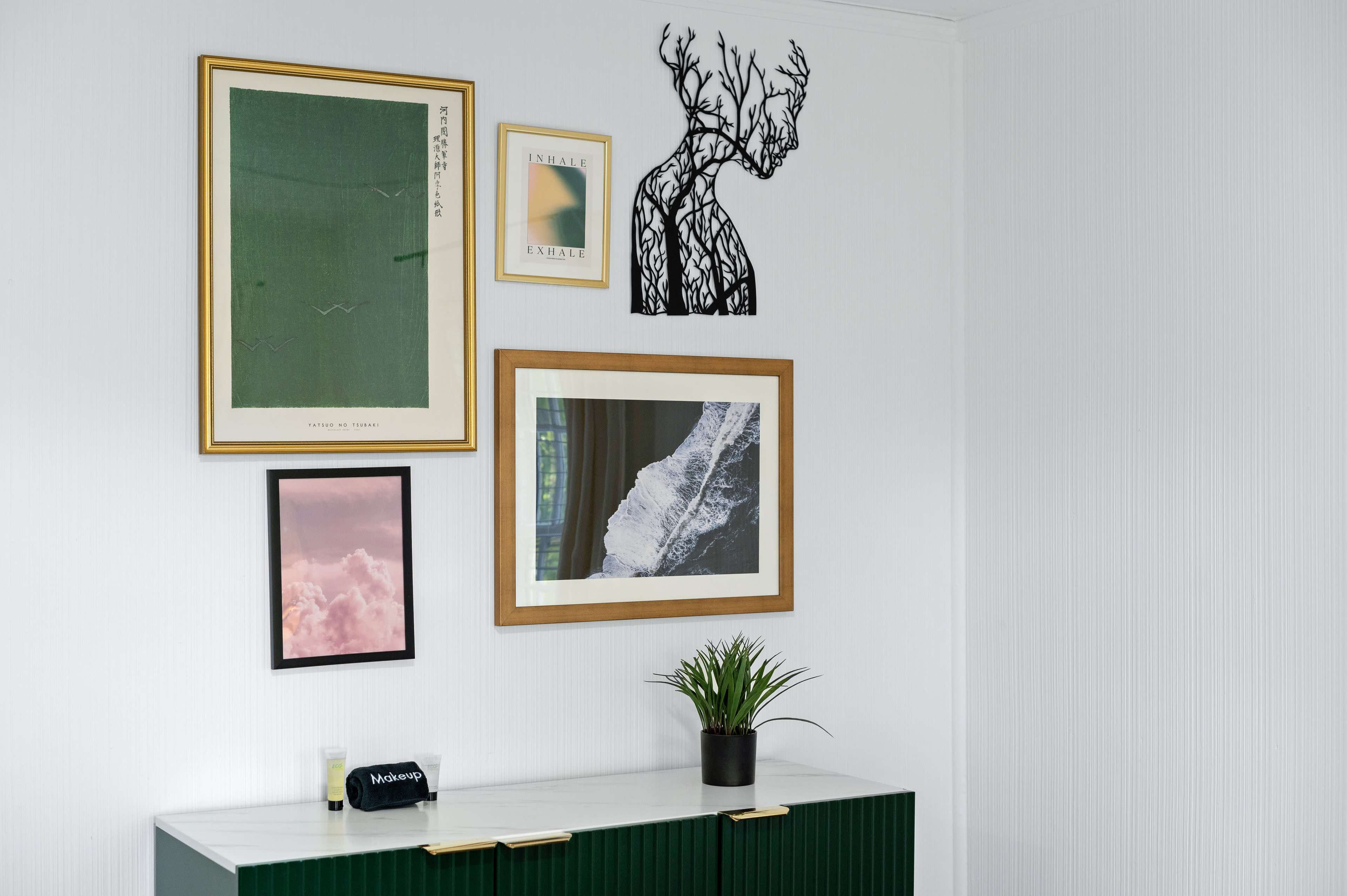 A wall adorned with various framed artworks and a small potted plant on a green cabinet.