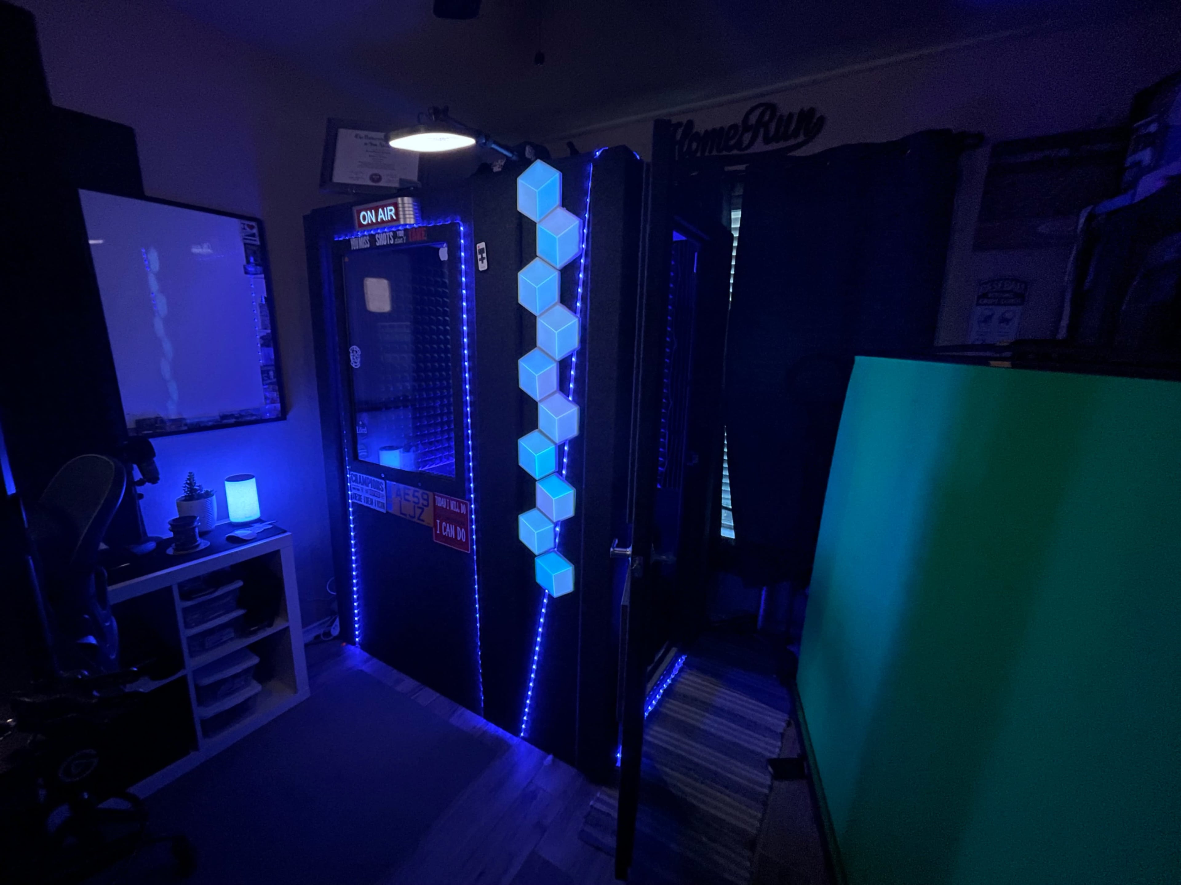 A dark room featuring a hexagon-patterned LED light installation next to a soundproof recording booth with an "ON AIR" sign.