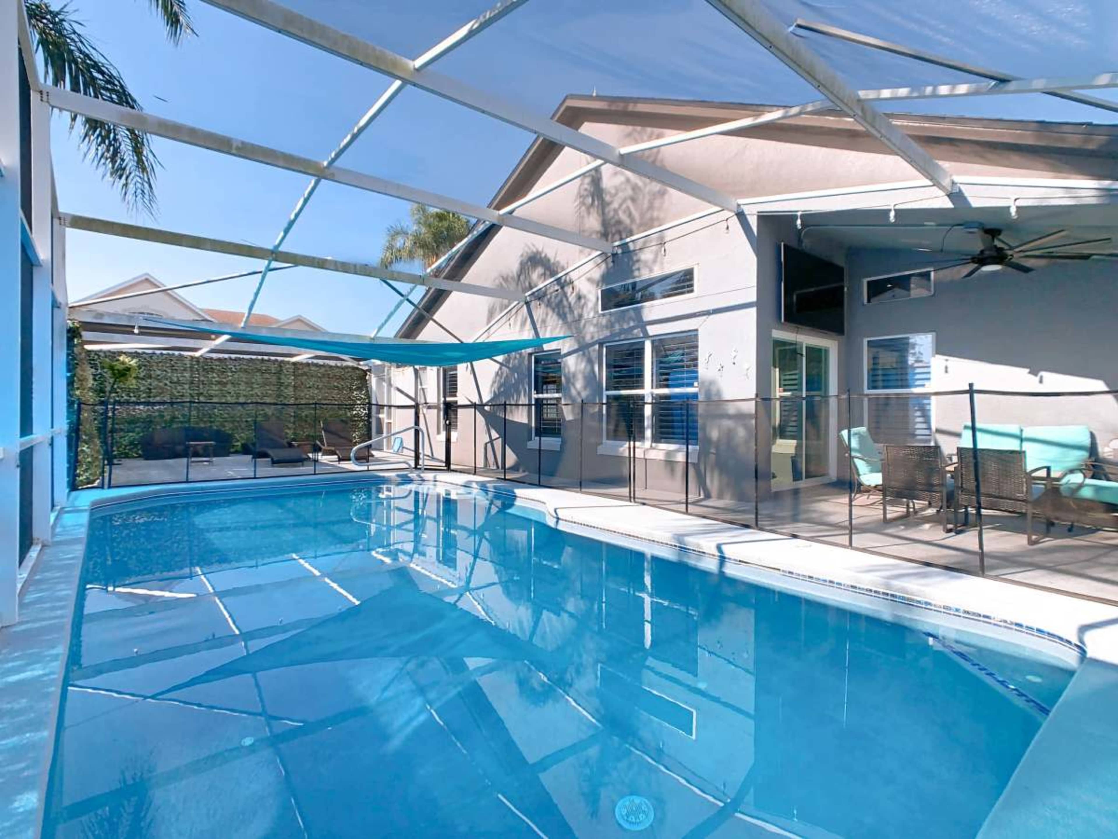 The image shows a screened-in swimming pool area with a clear blue pool and lounge chairs situated around it.