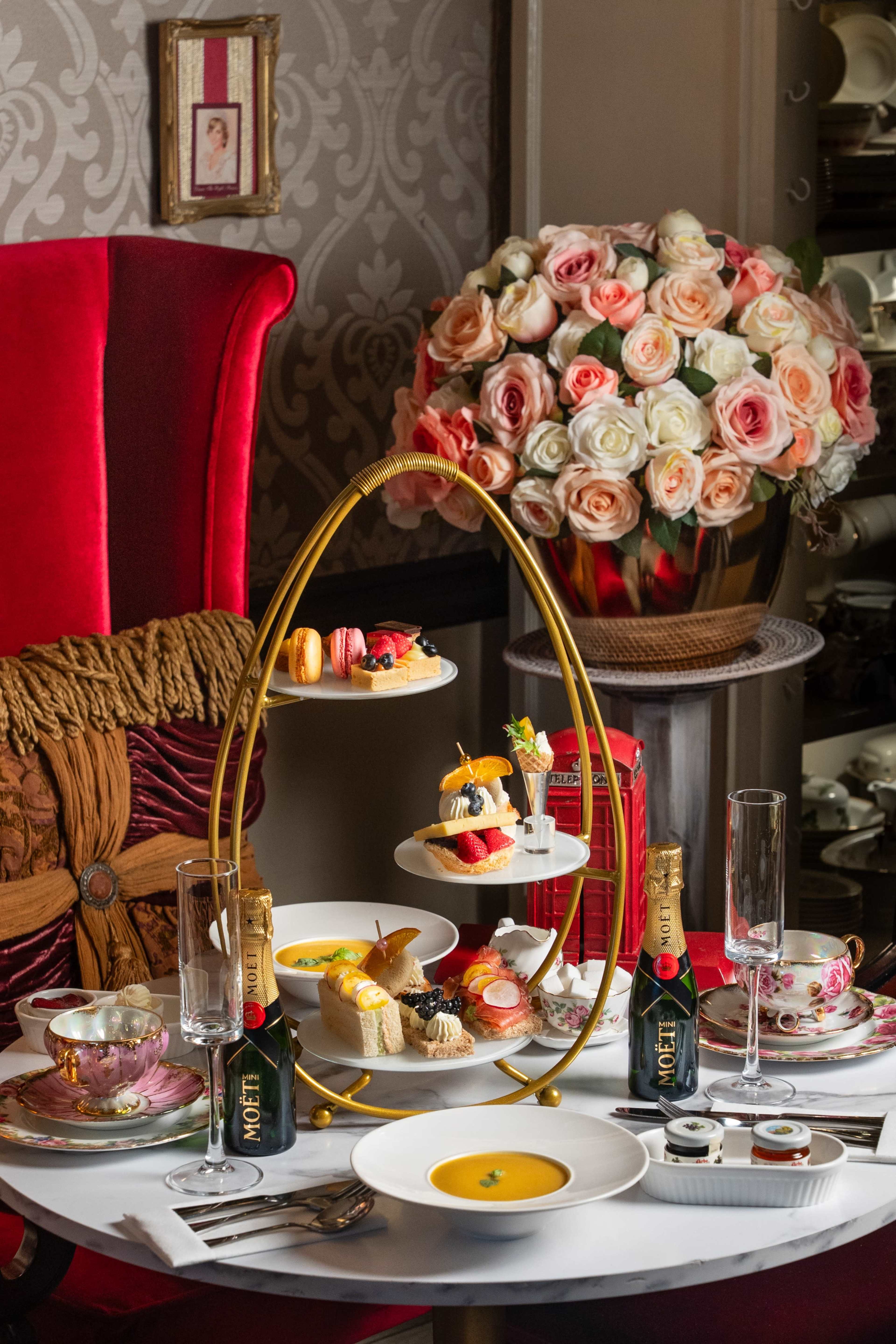 A beautifully arranged afternoon tea set is presented on a three-tier stand, surrounded by elegant tableware and a floral centerpiece.