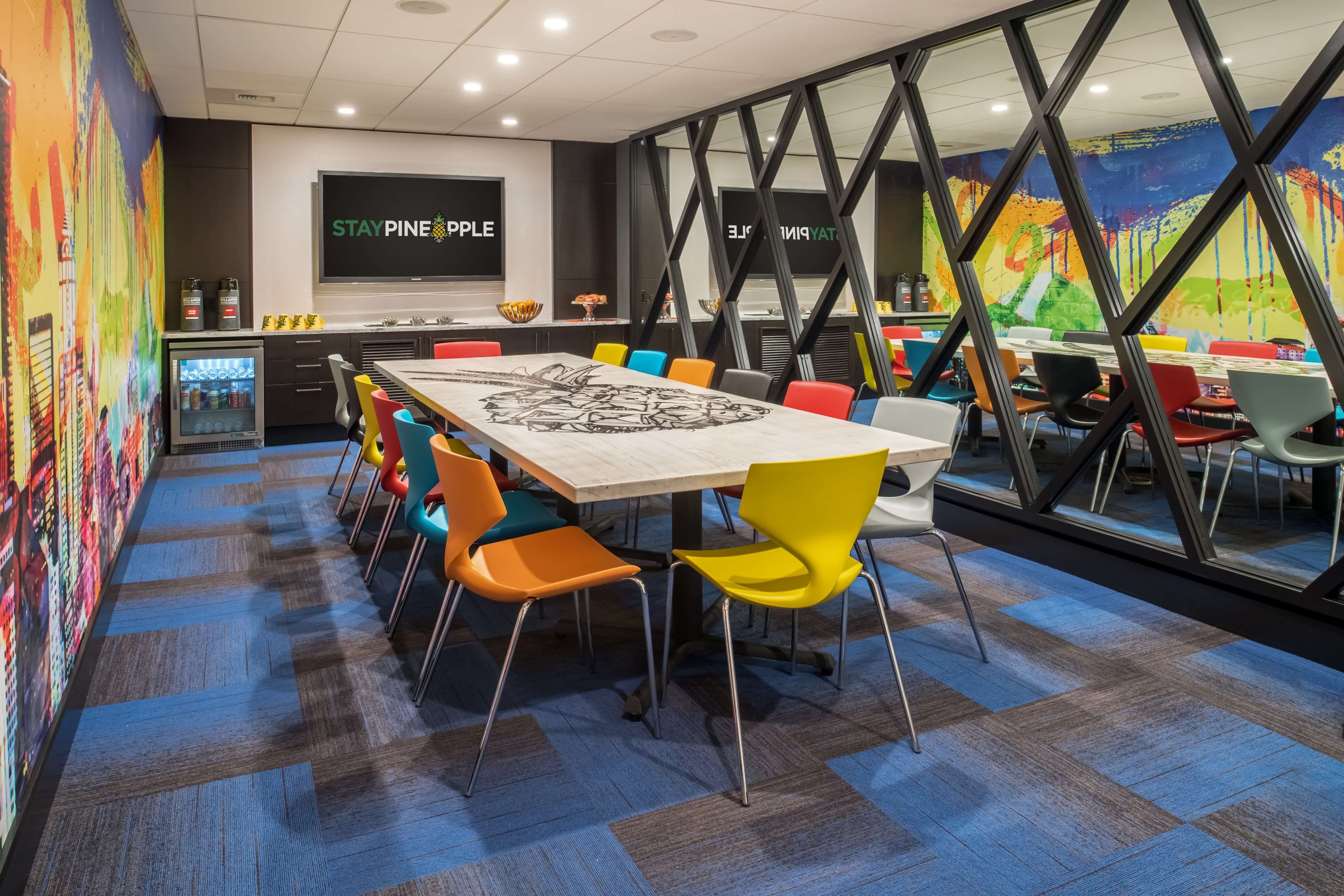 A modern conference room with a large table surrounded by colorful chairs and vibrant wall art.
