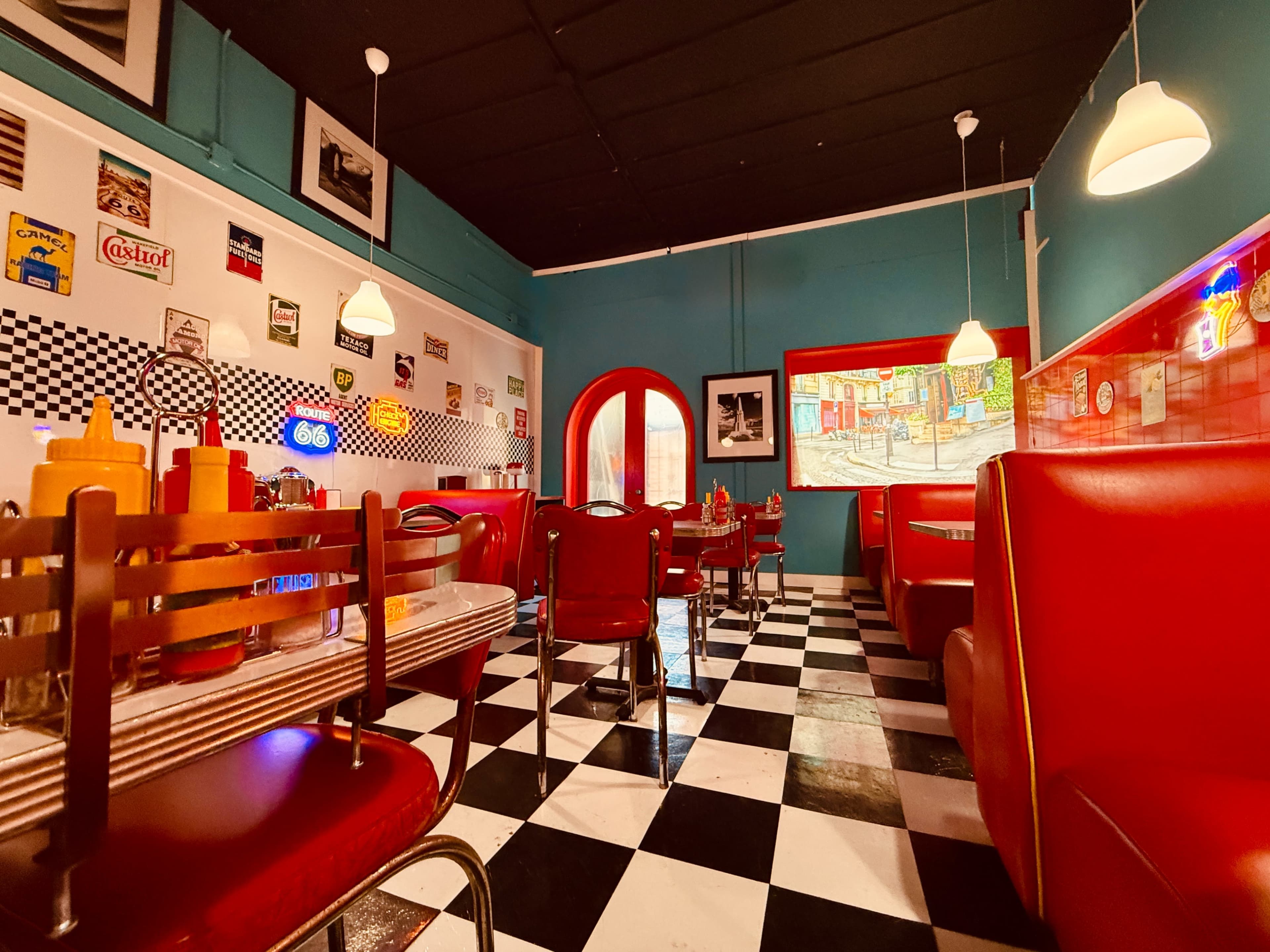 The image shows a retro diner interior with red vinyl seating, checkered floor tiles, and colorful wall decorations.