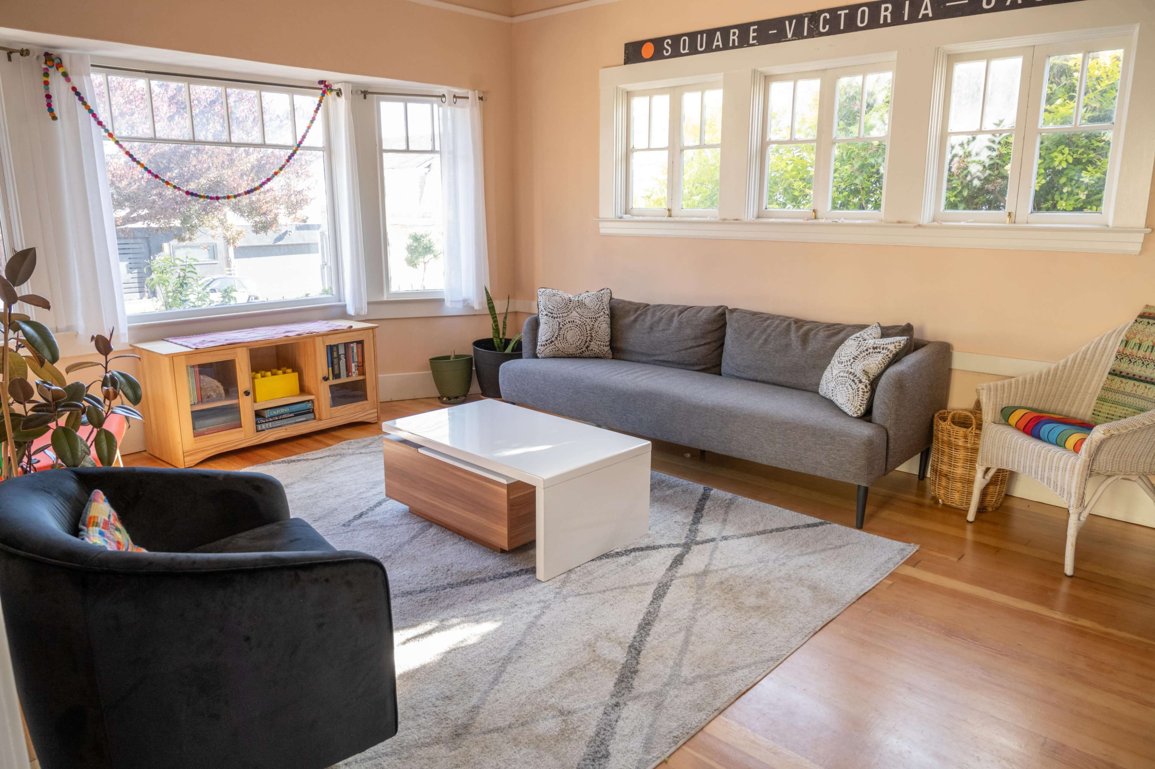 A bright living room with a gray sofa, a black armchair, a wooden coffee table, and large windows allowing natural light.