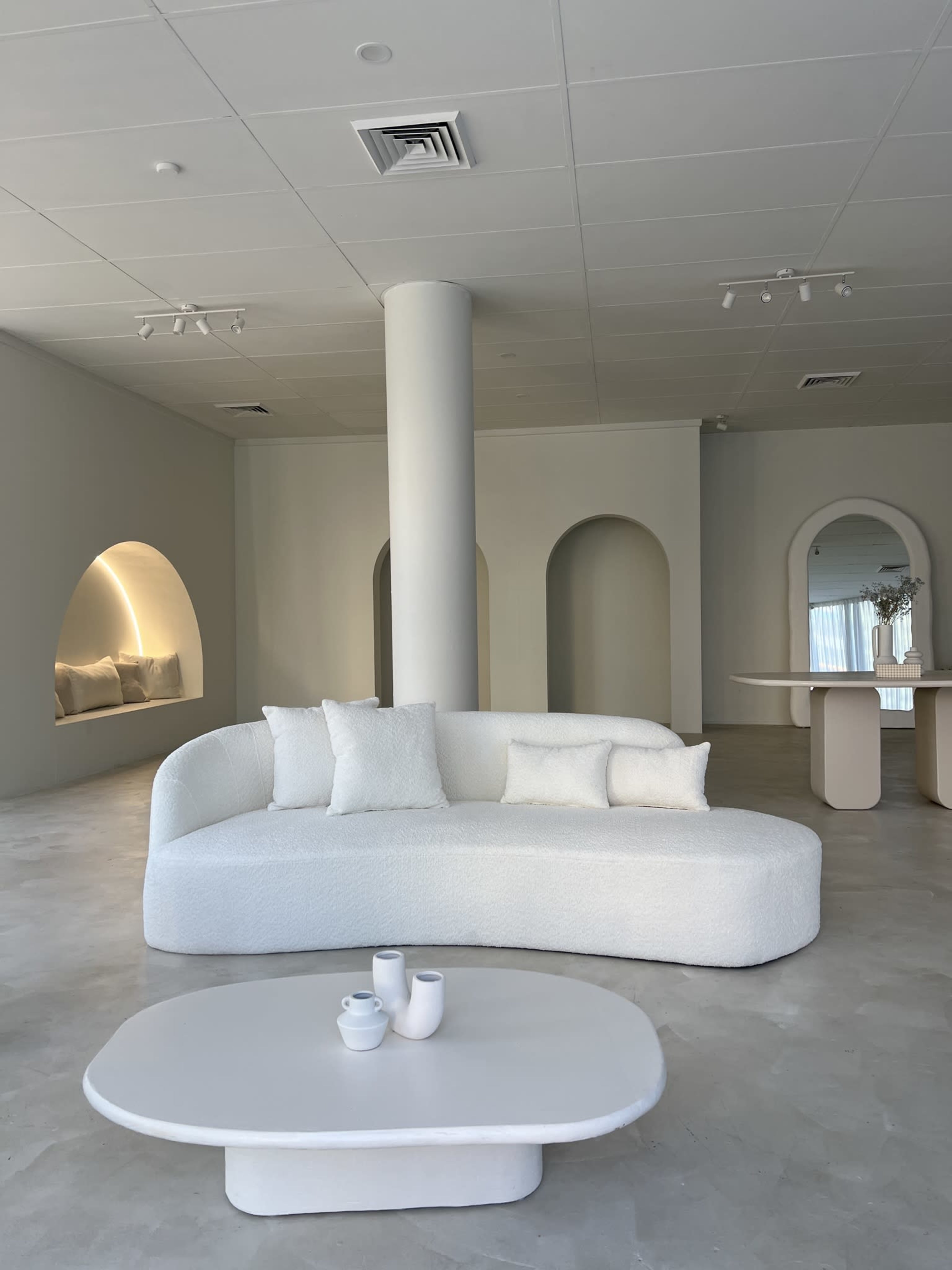 A modern, minimalist living space featuring a curved white sofa, a round coffee table, and arched wall niches illuminated softly.