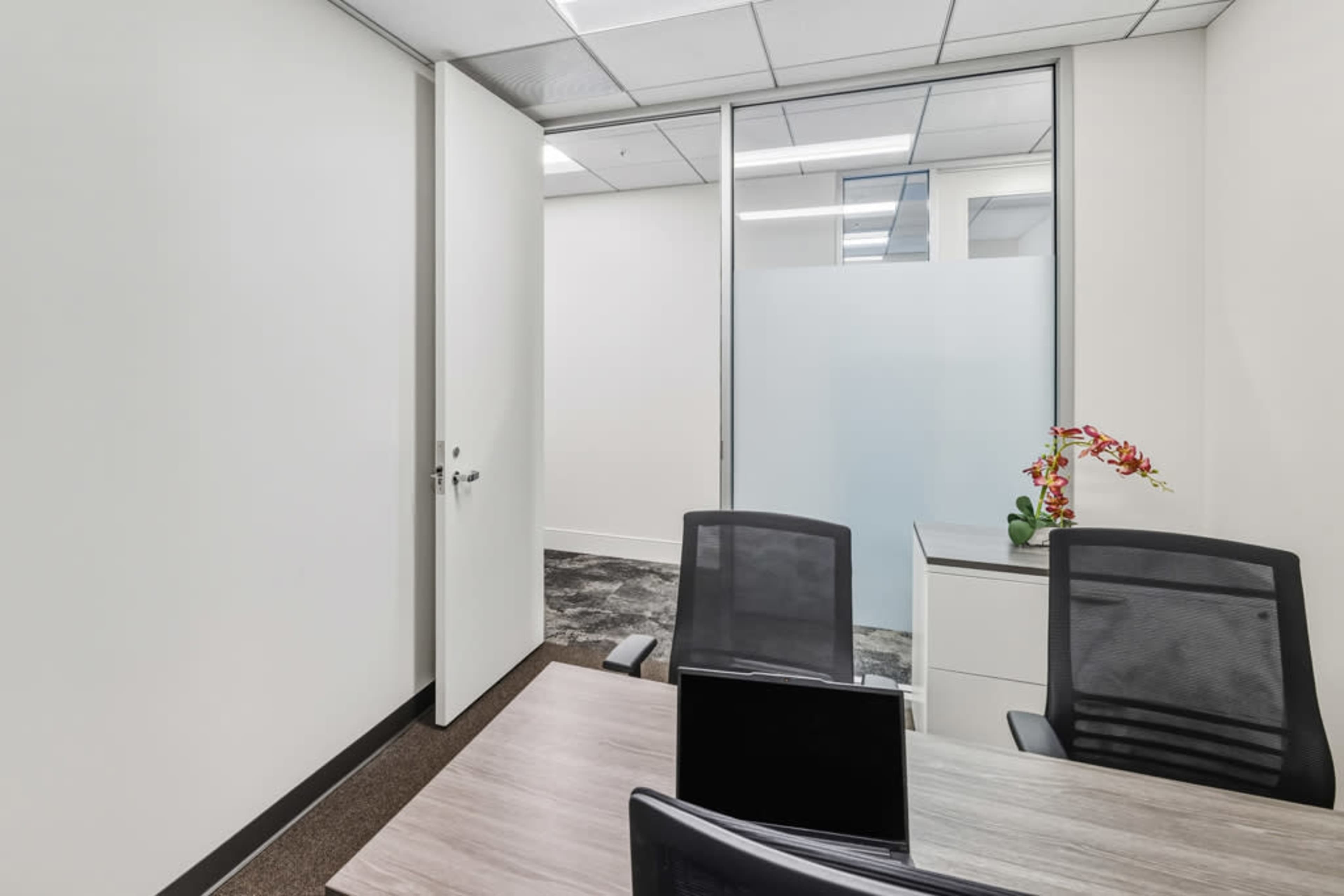 The image shows a modern office space with a table, two chairs, and a partially open door leading to another room.