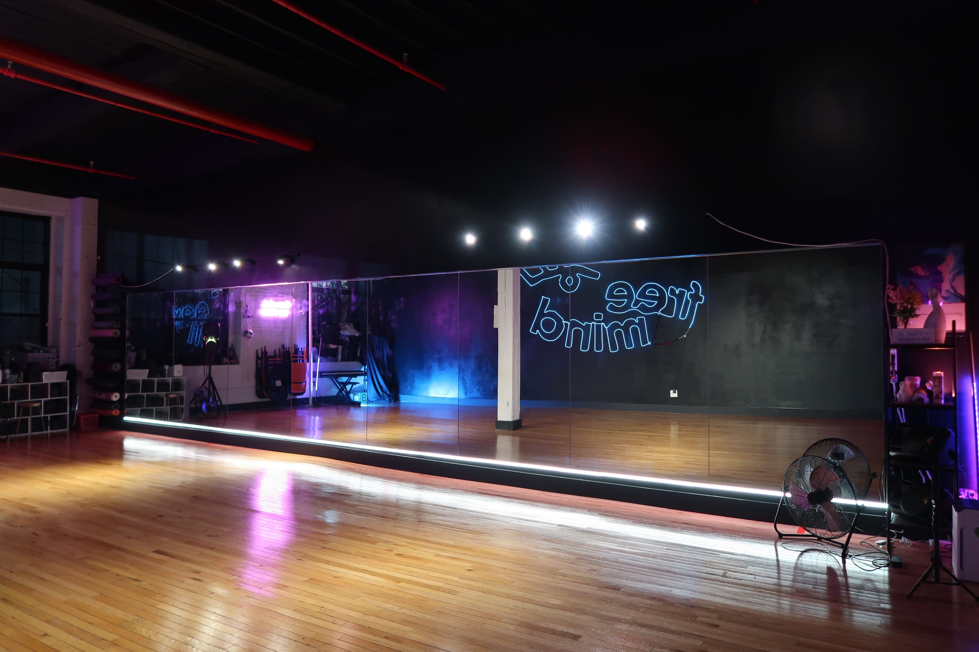 The image shows a spacious dance studio with a large wall mirror and illuminated lighting effects in a dark setting.
