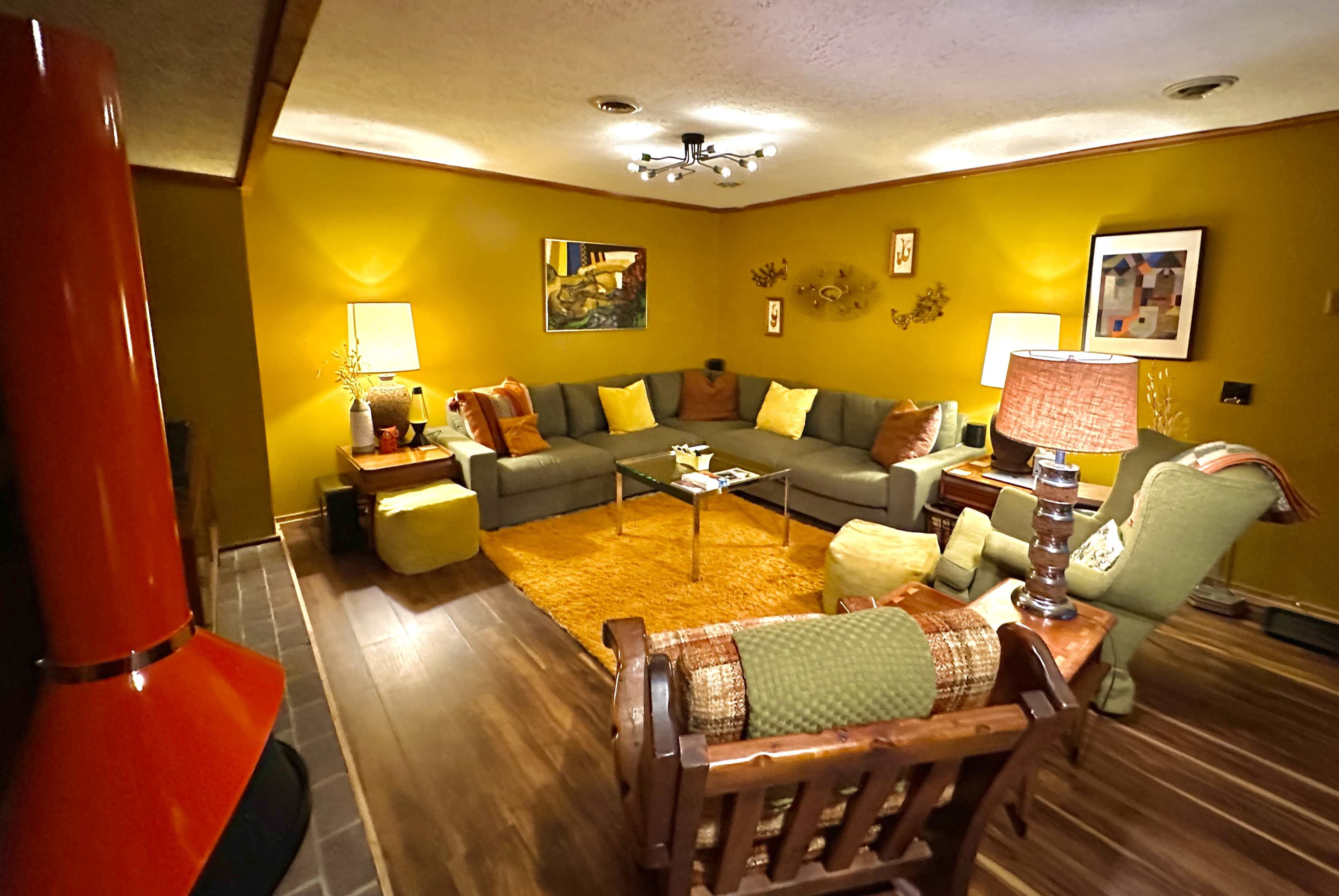 A cozy living room with green walls, a sectional sofa, and a coffee table placed on a light orange rug.