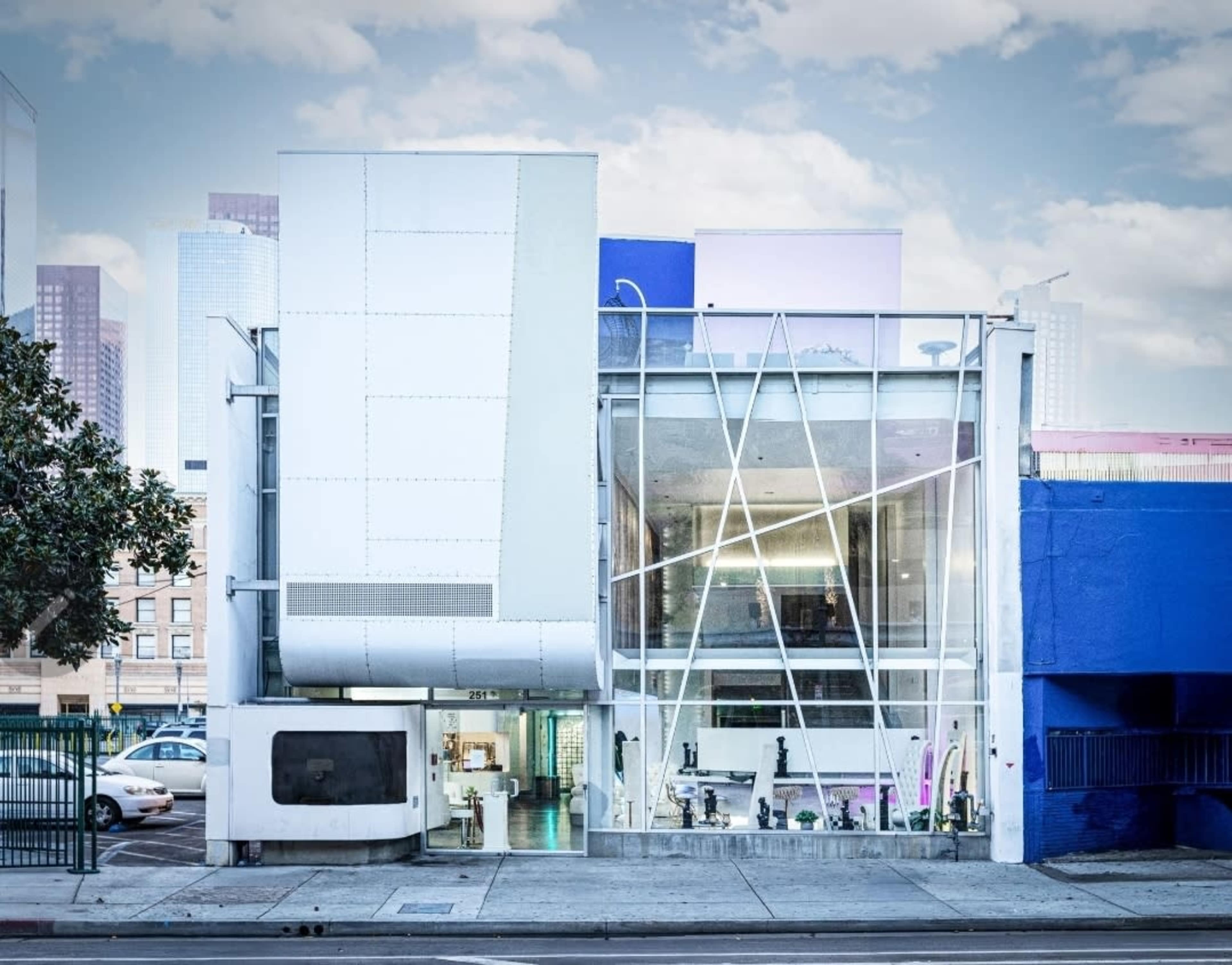The image shows a modern building with a distinct geometric facade featuring glass and metal elements, located in an urban setting.