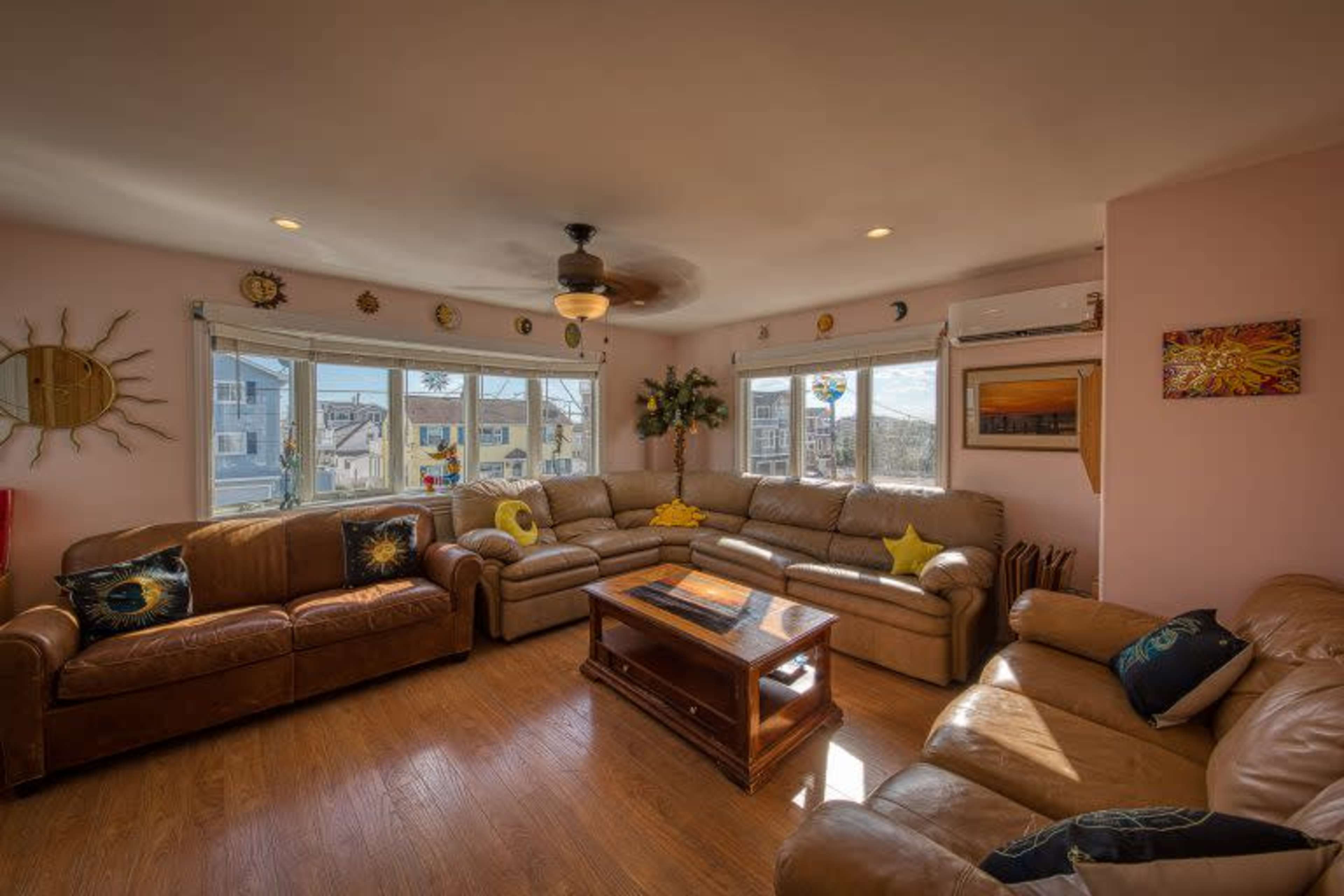 The living room features several leather sofas arranged around a wooden coffee table, with large windows allowing natural light to fill the space.