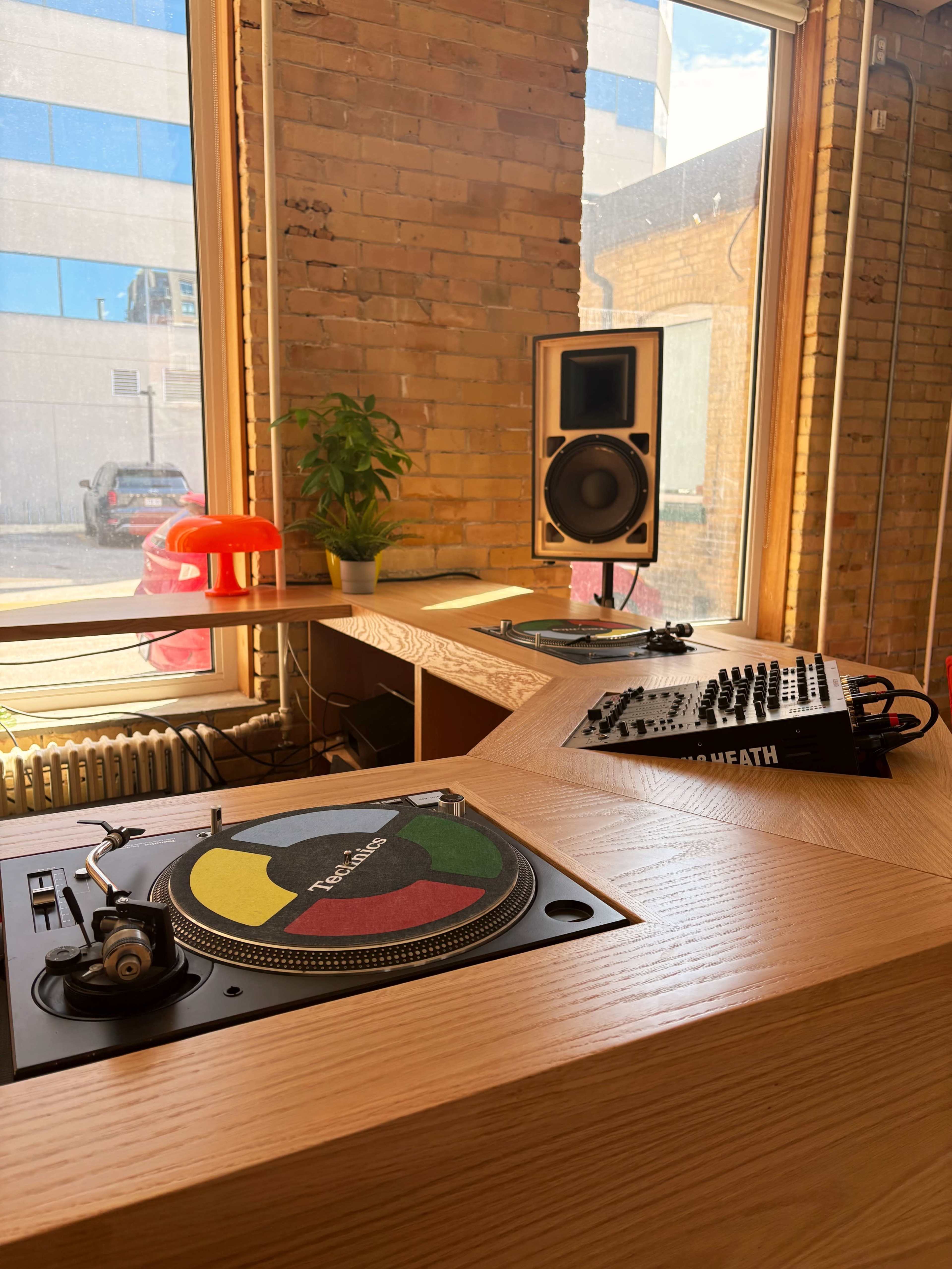 A modern music setup featuring a turntable, a DJ mixer, and a studio monitor in a well-lit room with large windows.