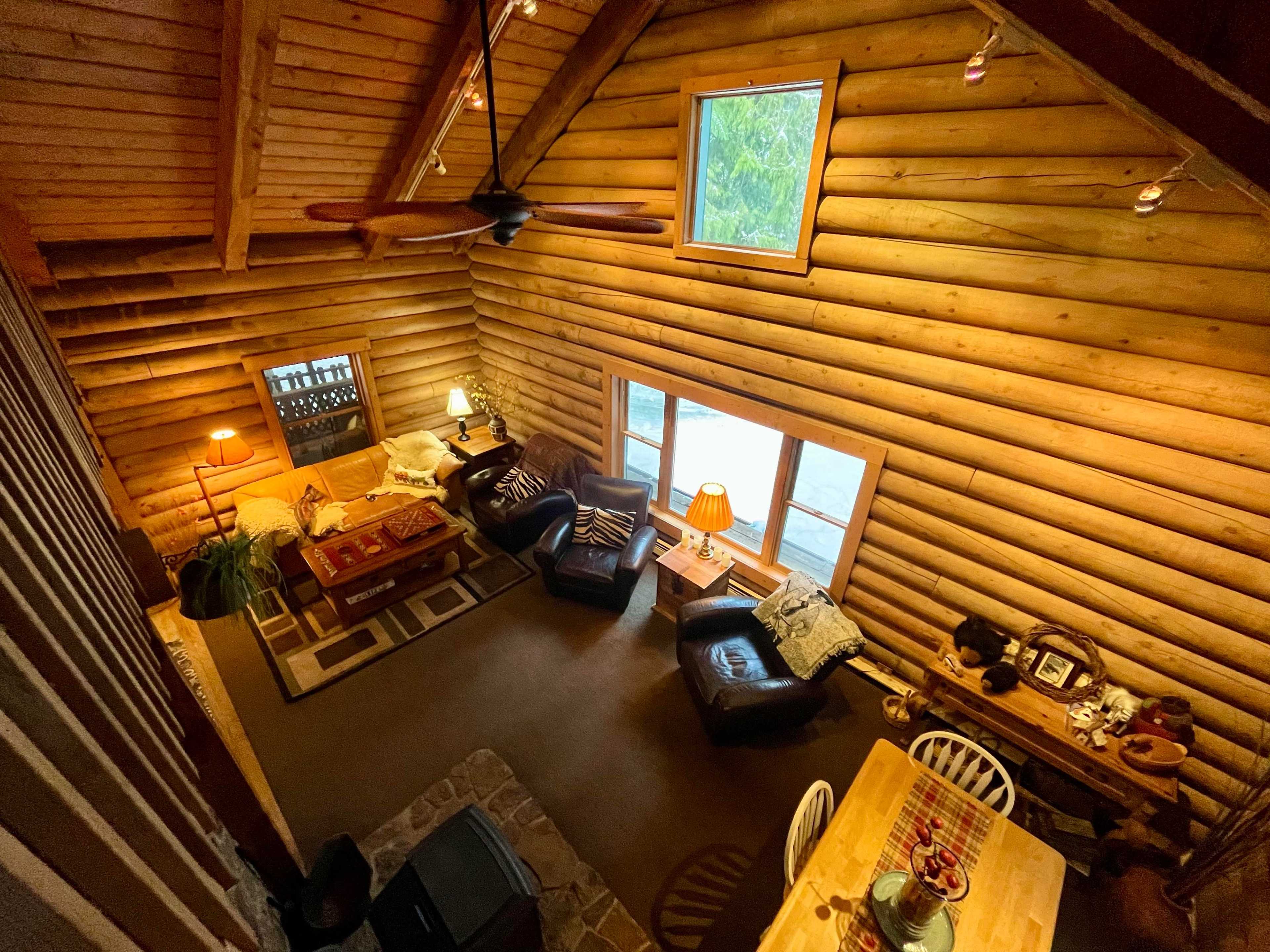 A cabin-style living room with wooden walls, a seating area with leather chairs, and a dining table.