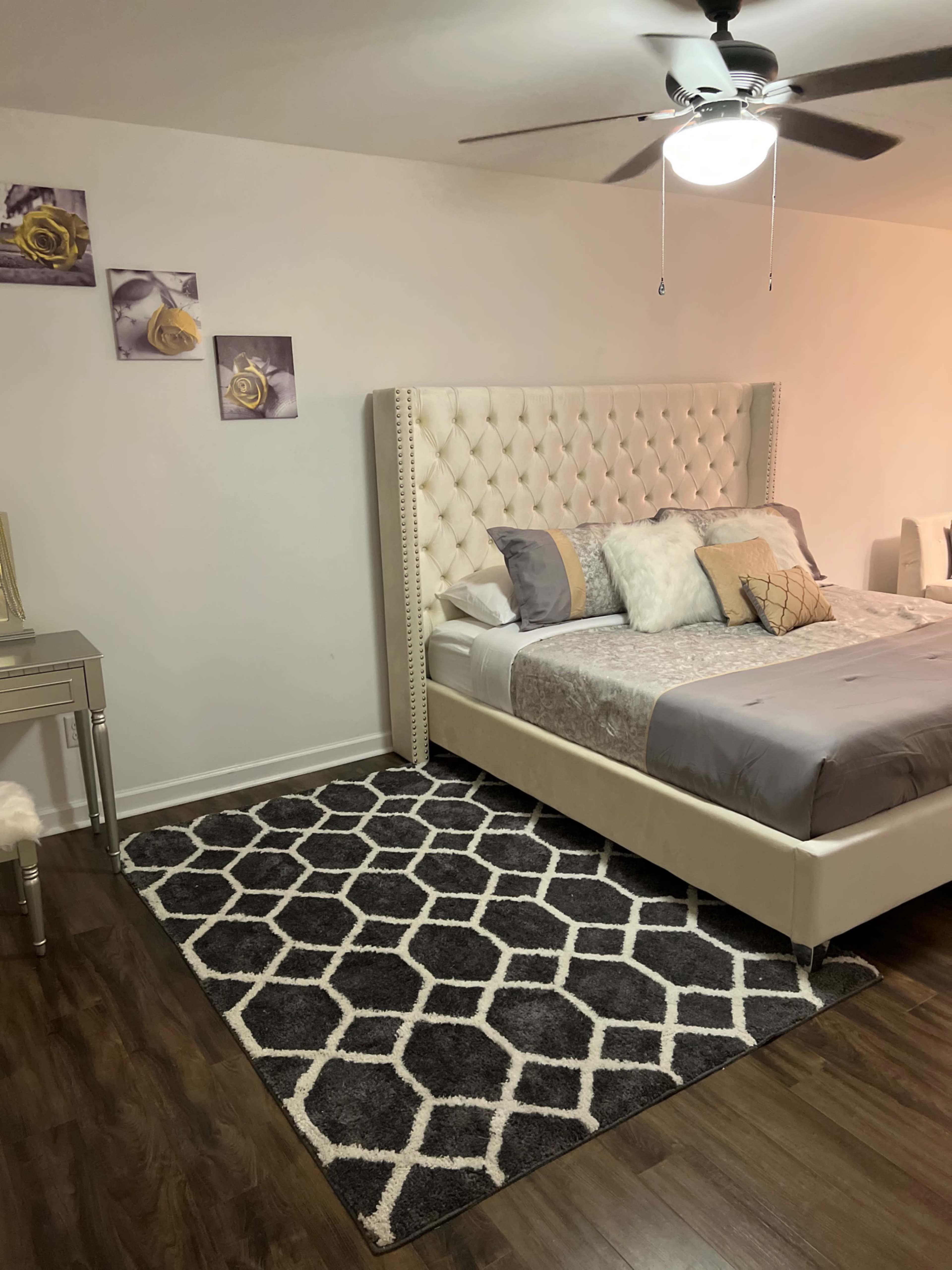 A modern bedroom featuring a tufted white bed frame, a gray patterned rug, and wall art above the bed.