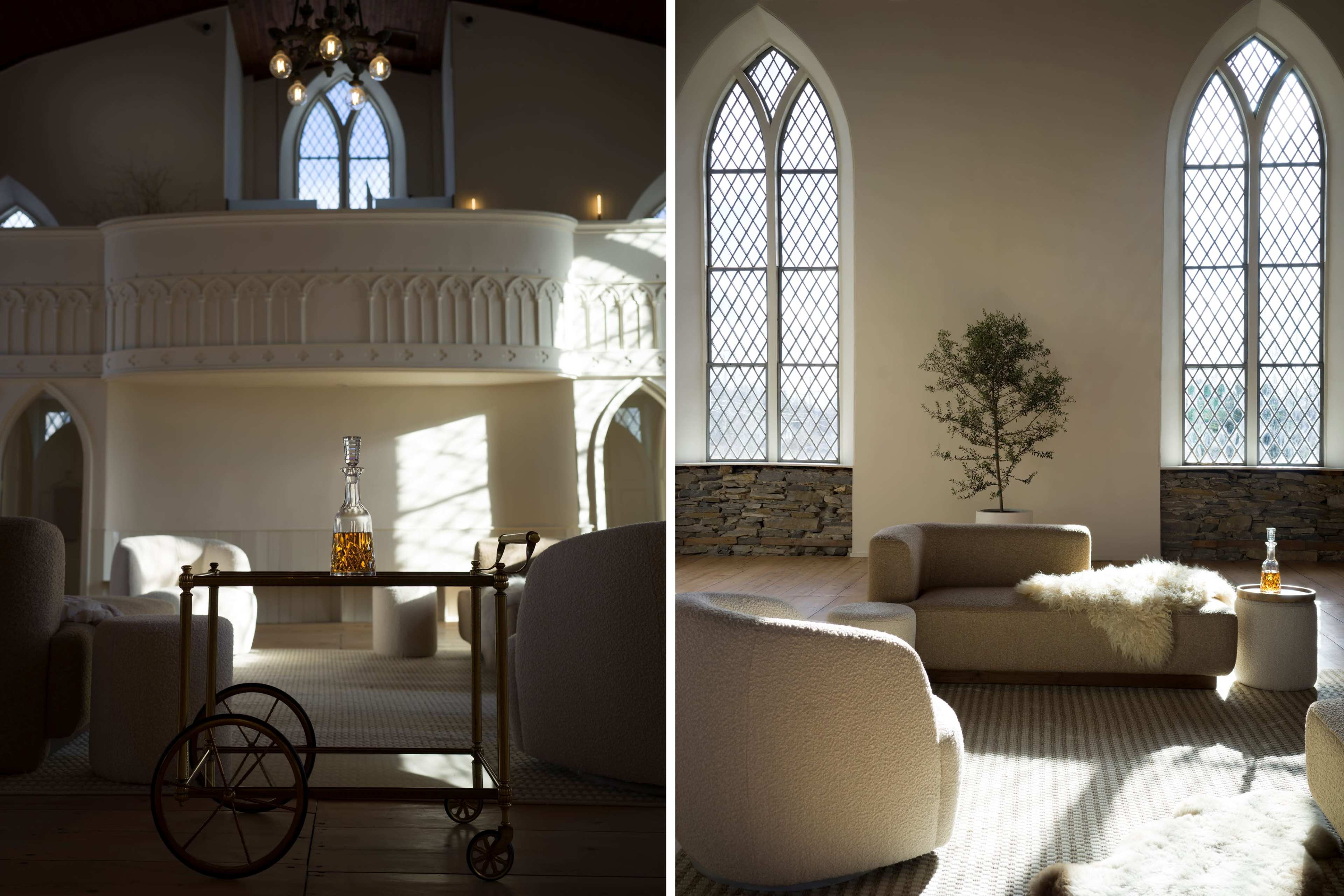 A spacious room with high ceilings, large arched windows, and modern furniture, including a circular coffee table with a bottle and a small tree in the corner.