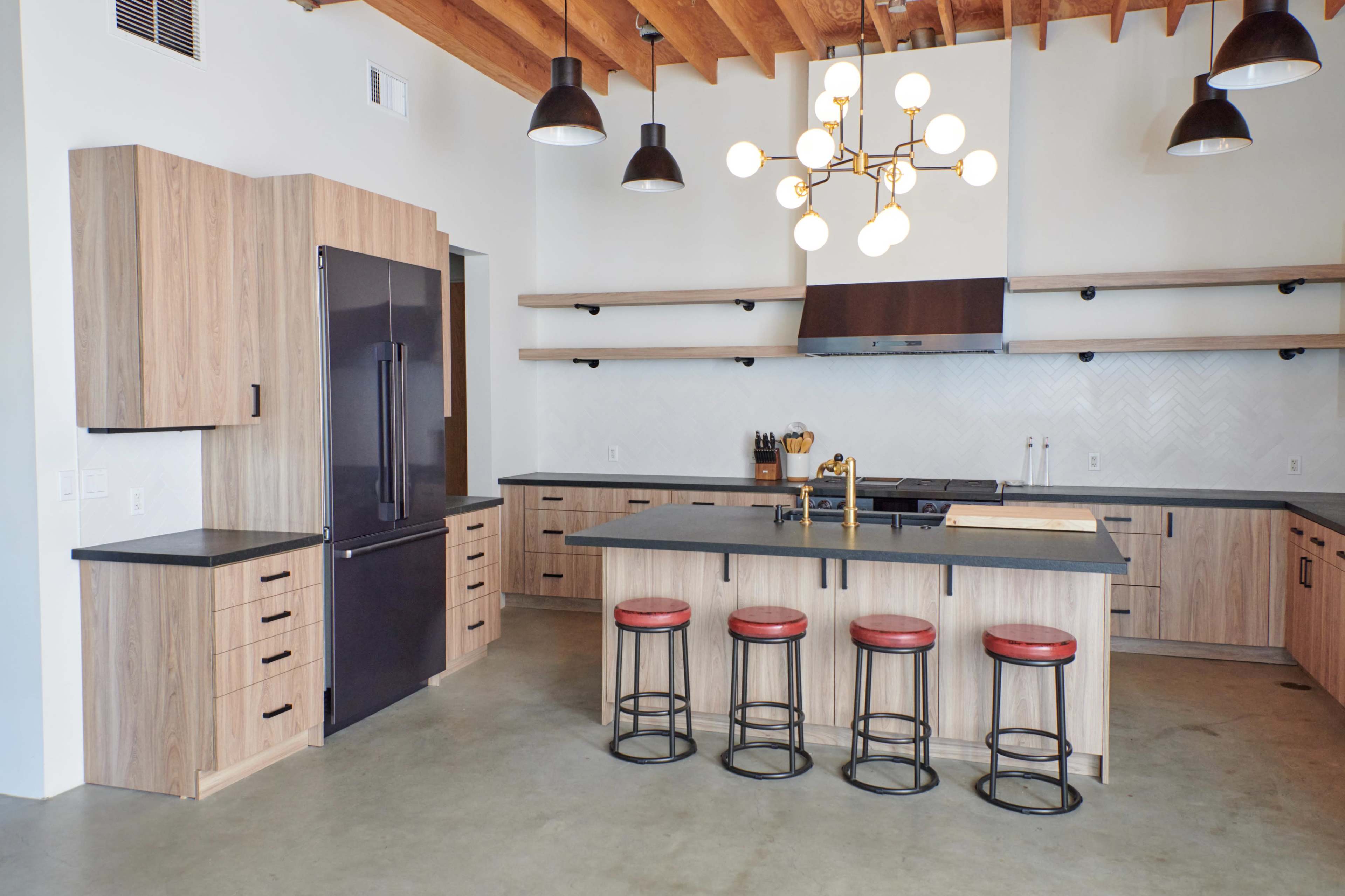 The image shows a modern kitchen featuring wooden cabinetry, a large island with seating, and contemporary light fixtures.
