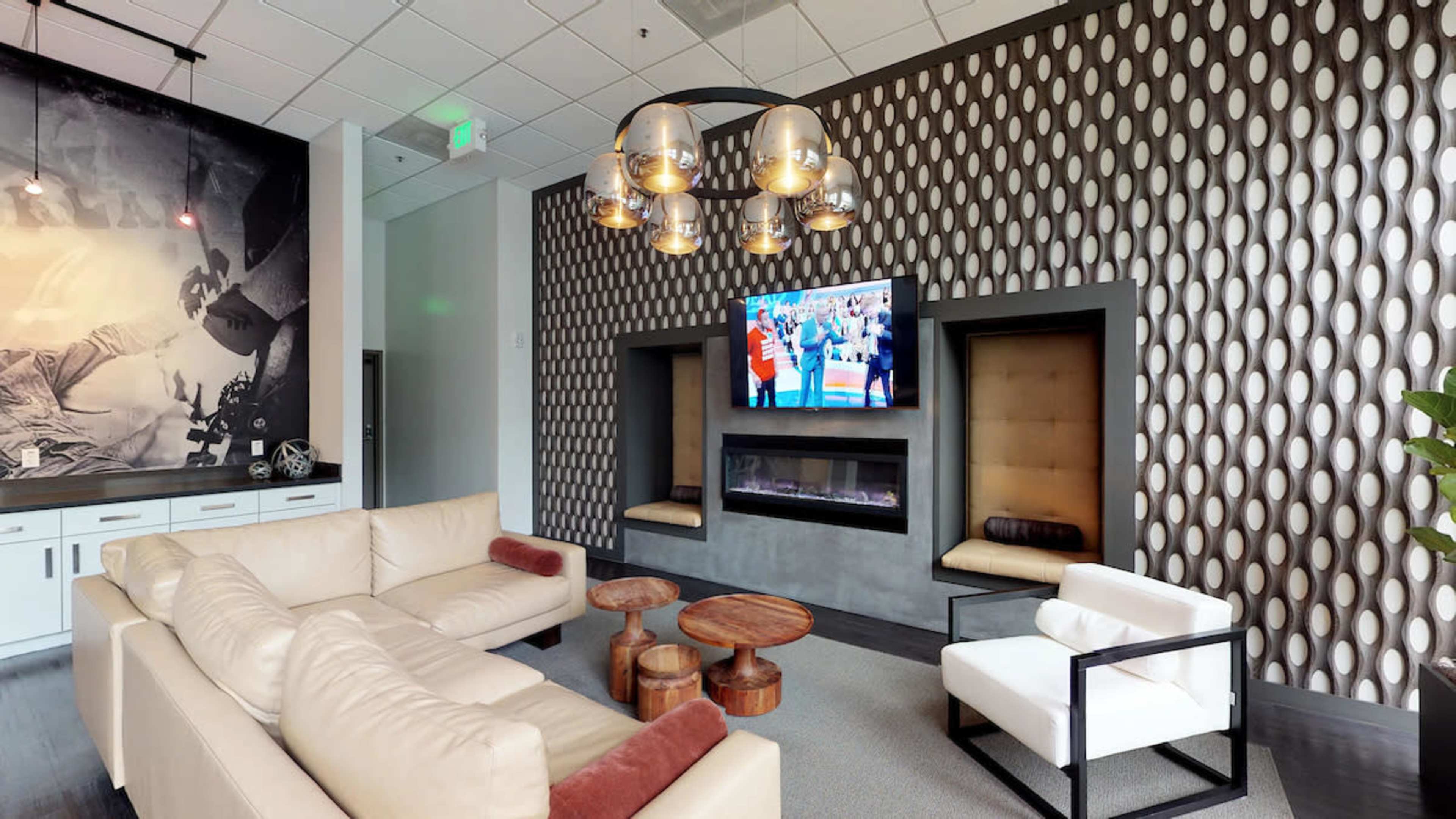 A modern lounge area featuring a light-colored sofa, a black and white television screen on the wall, and two contemporary fireplace structures.