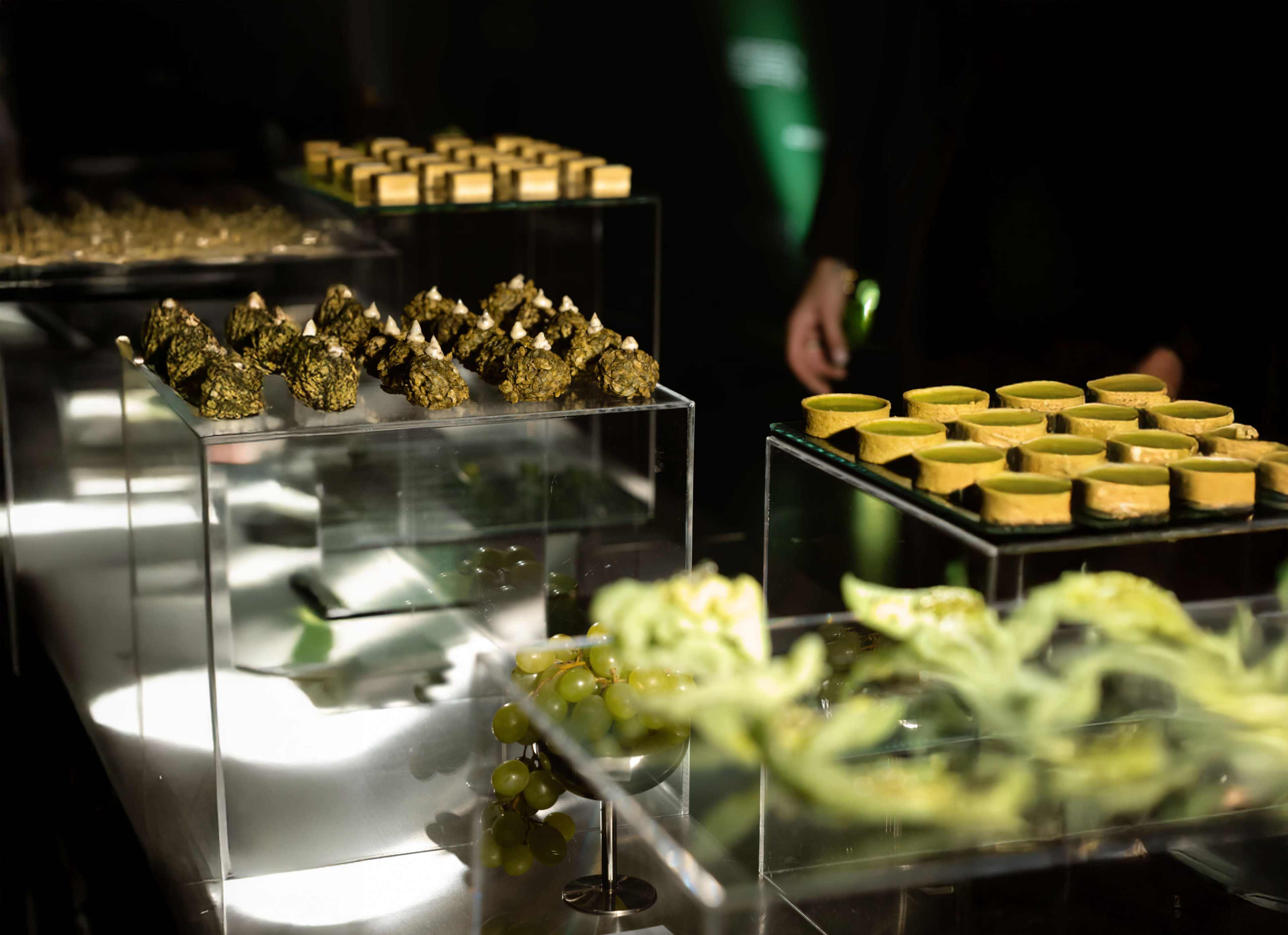 The image features an assortment of neatly arranged gourmet food items displayed on clear serving trays.