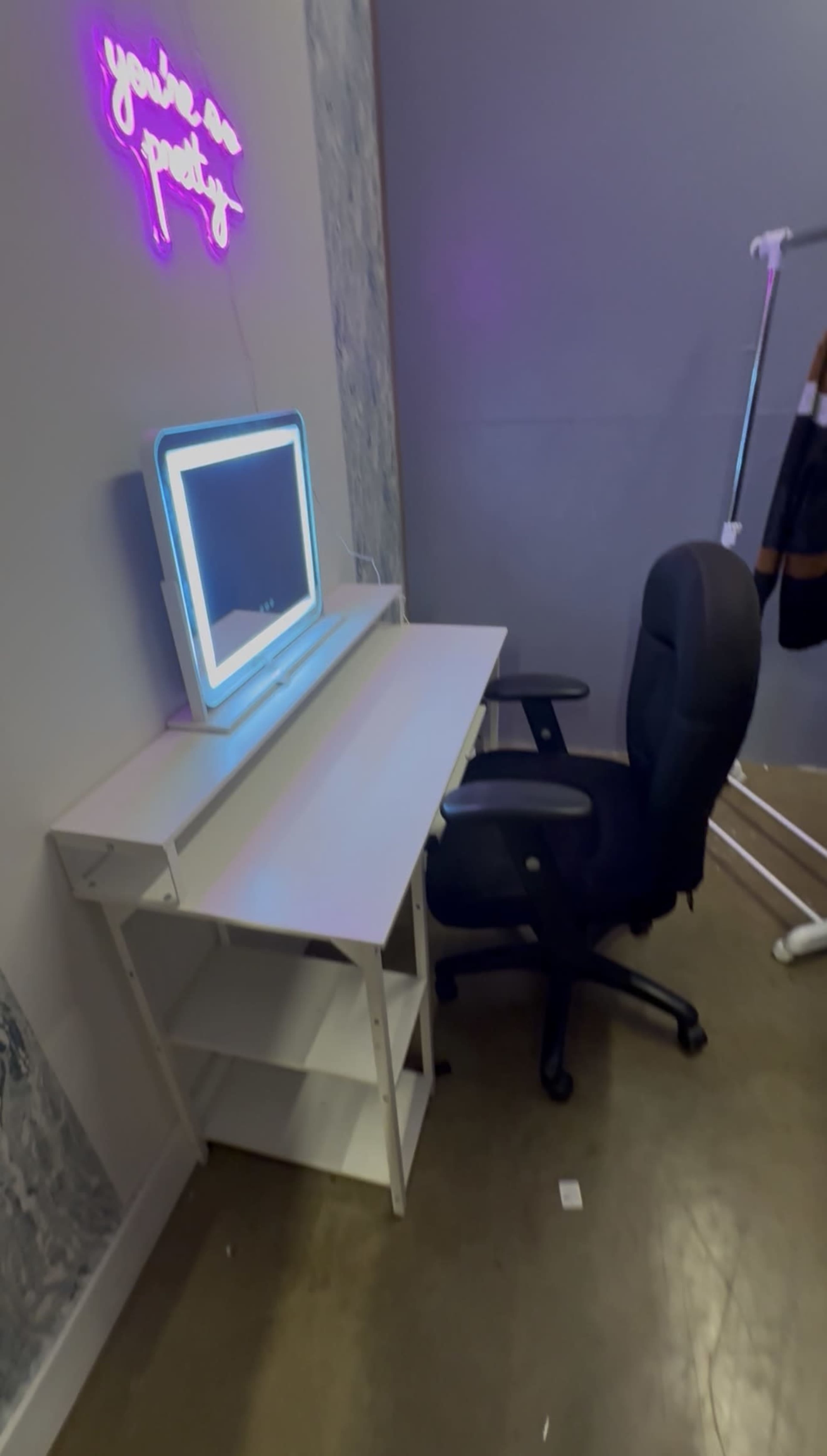 The image shows a white desk with a mirror and chair, positioned against a wall with a neon sign that reads "you're so pretty."