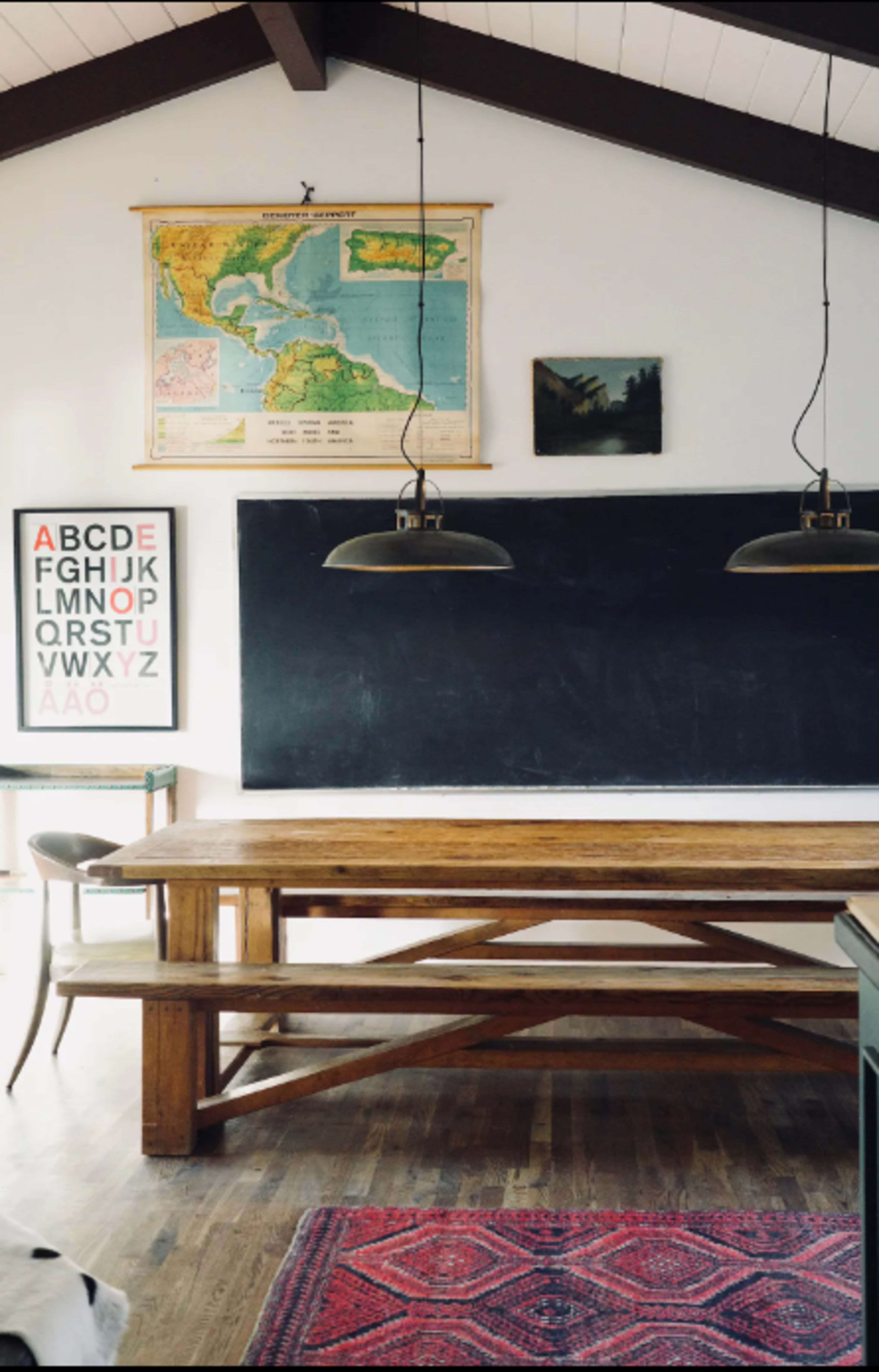 A simple classroom setting featuring a large wooden table, a black chalkboard, a map of the Caribbean on the wall, and two pendant lights hanging above the table.