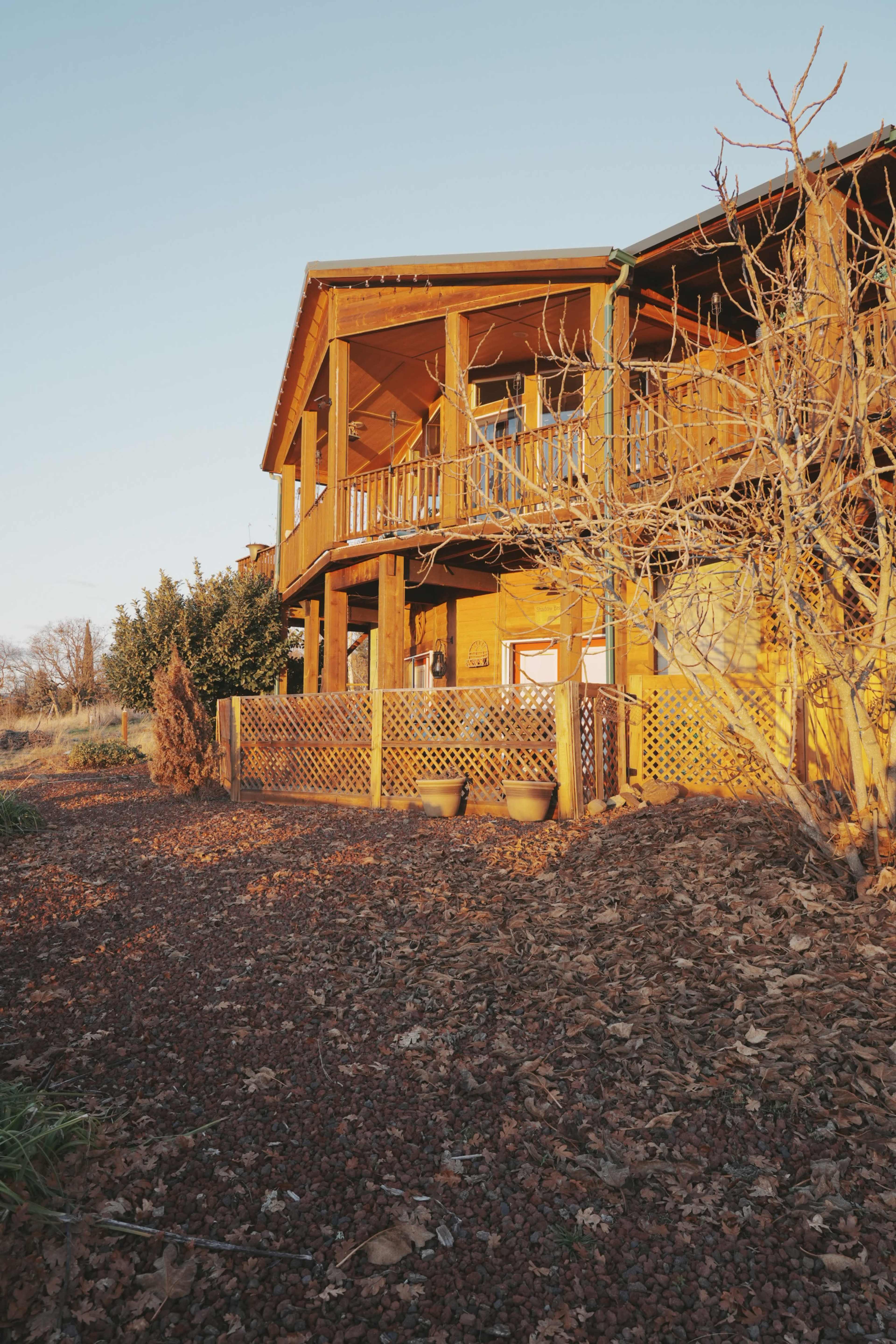 A wooden house with a porch overlooks a landscaped area featuring gravel and shrubs.