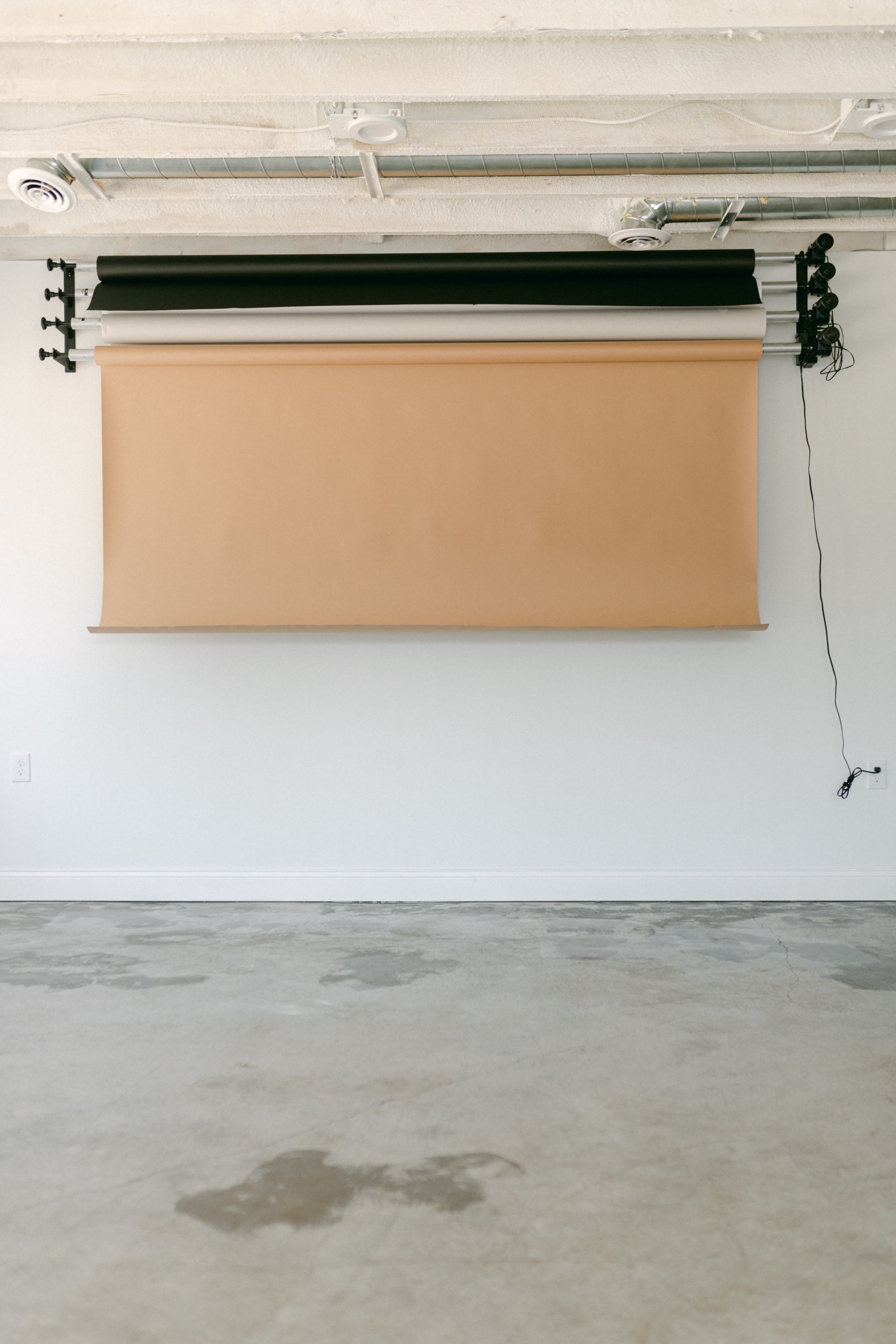 A blank backdrop mounted on a wall in a sparsely furnished studio space with a concrete floor.