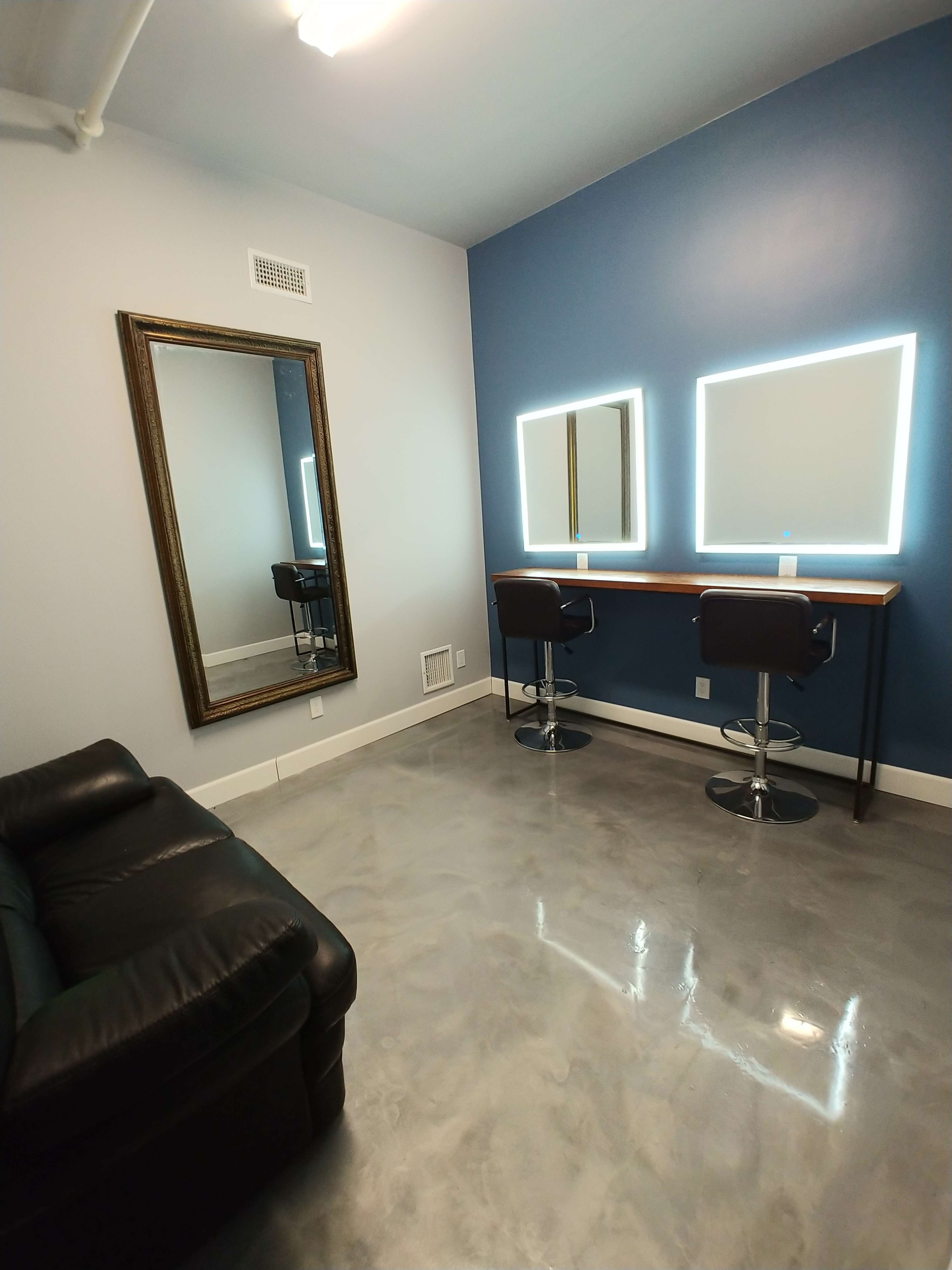 The image shows a modern room with two illuminated mirrors above a wooden table and a black leather couch beside a decorative wall mirror.