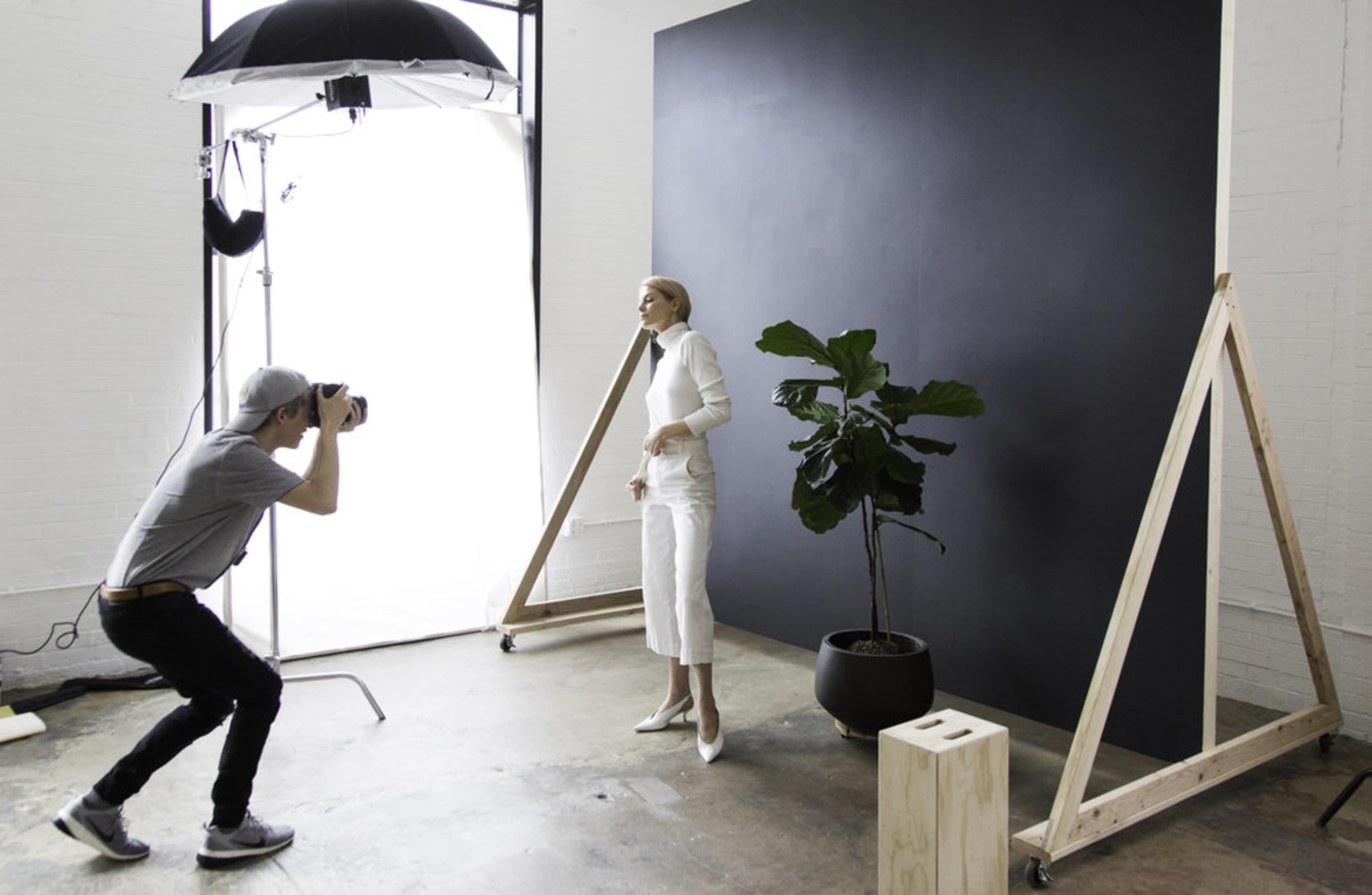 A photographer captures an image of a model posing in front of a black backdrop in a studio setting.