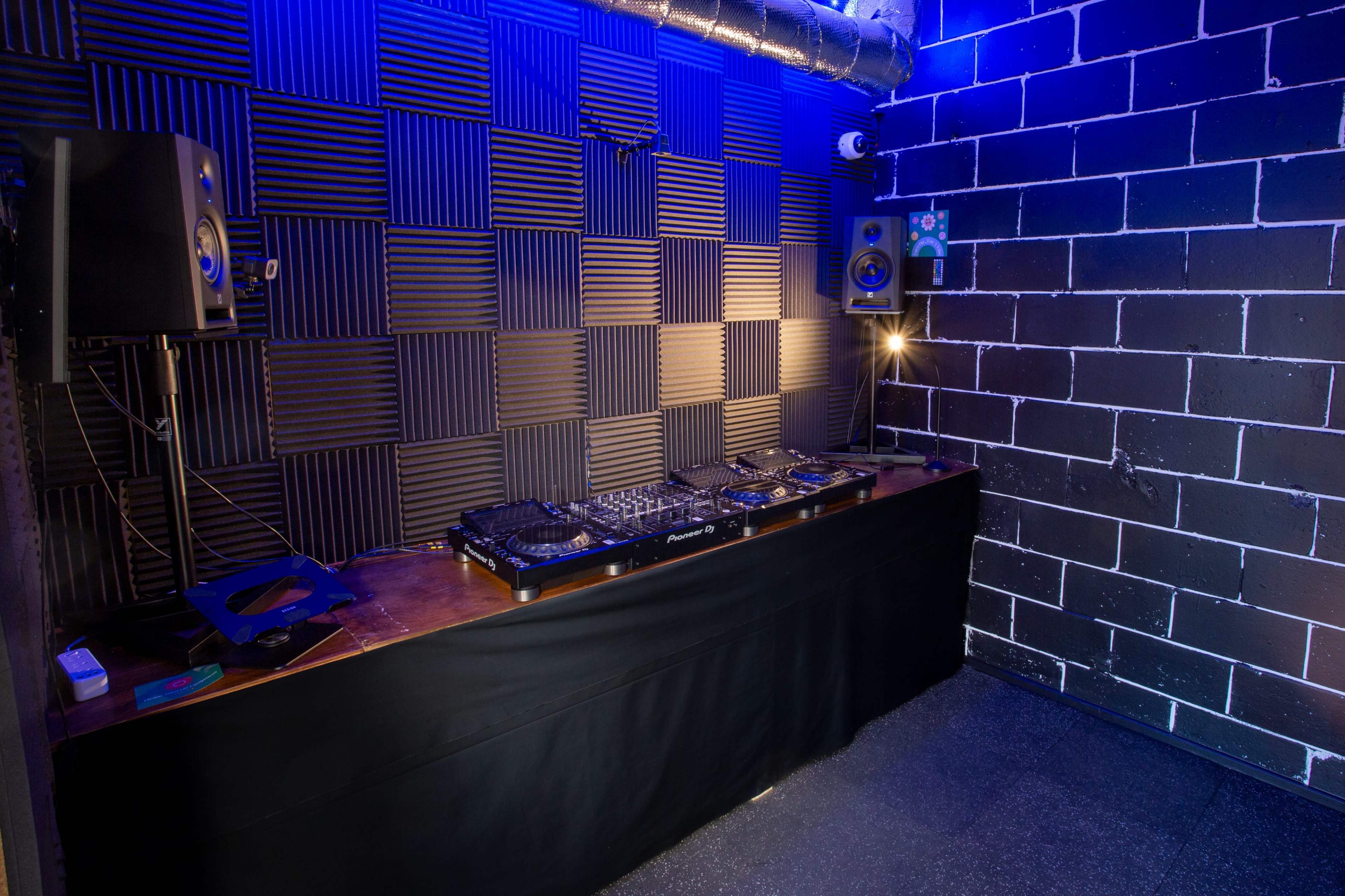A DJ booth with a mixer and speakers in a soundproof room featuring black padded walls and dim lighting.