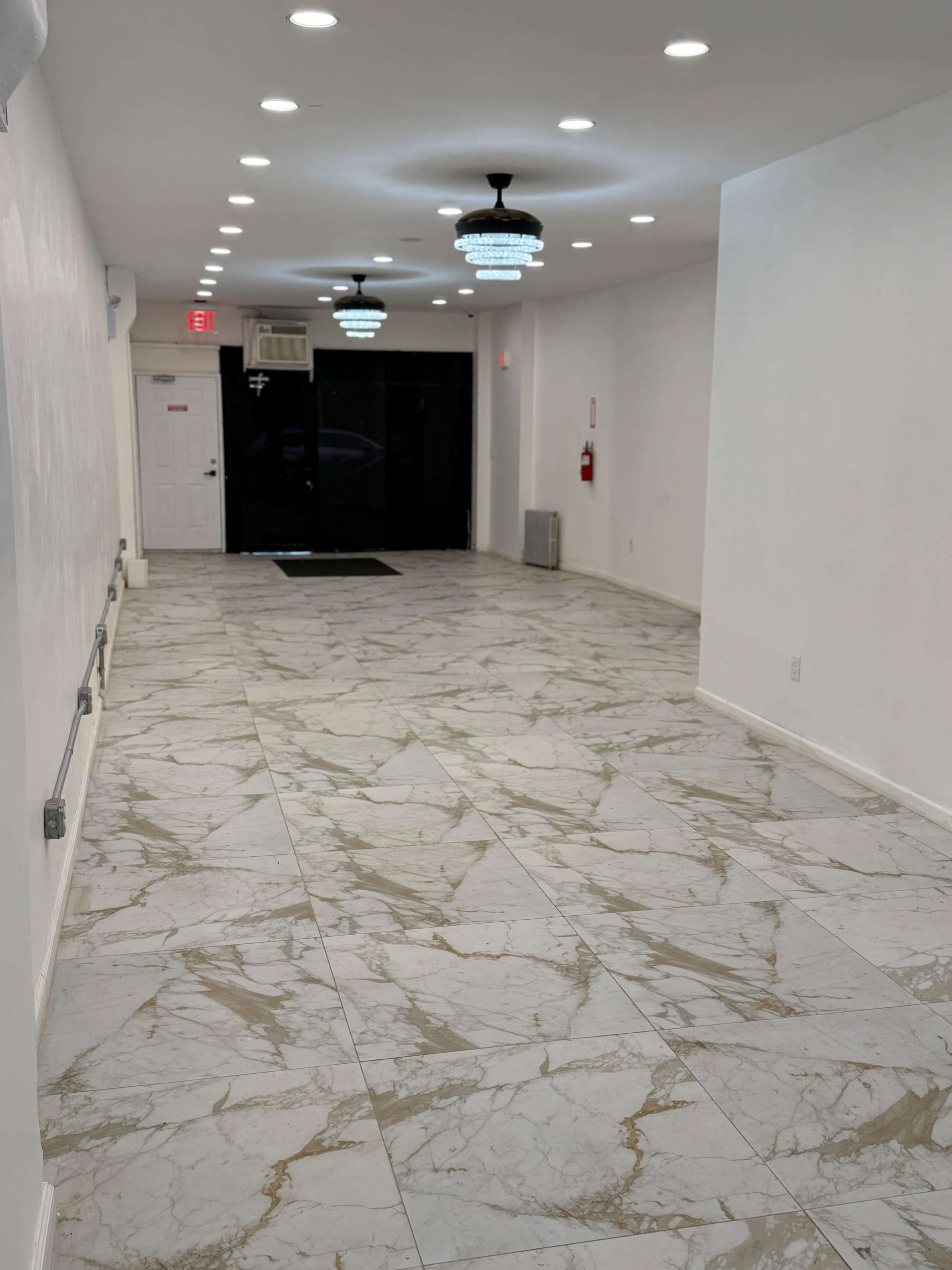 The image shows a long, well-lit hallway with marble flooring and decorative ceiling lights.