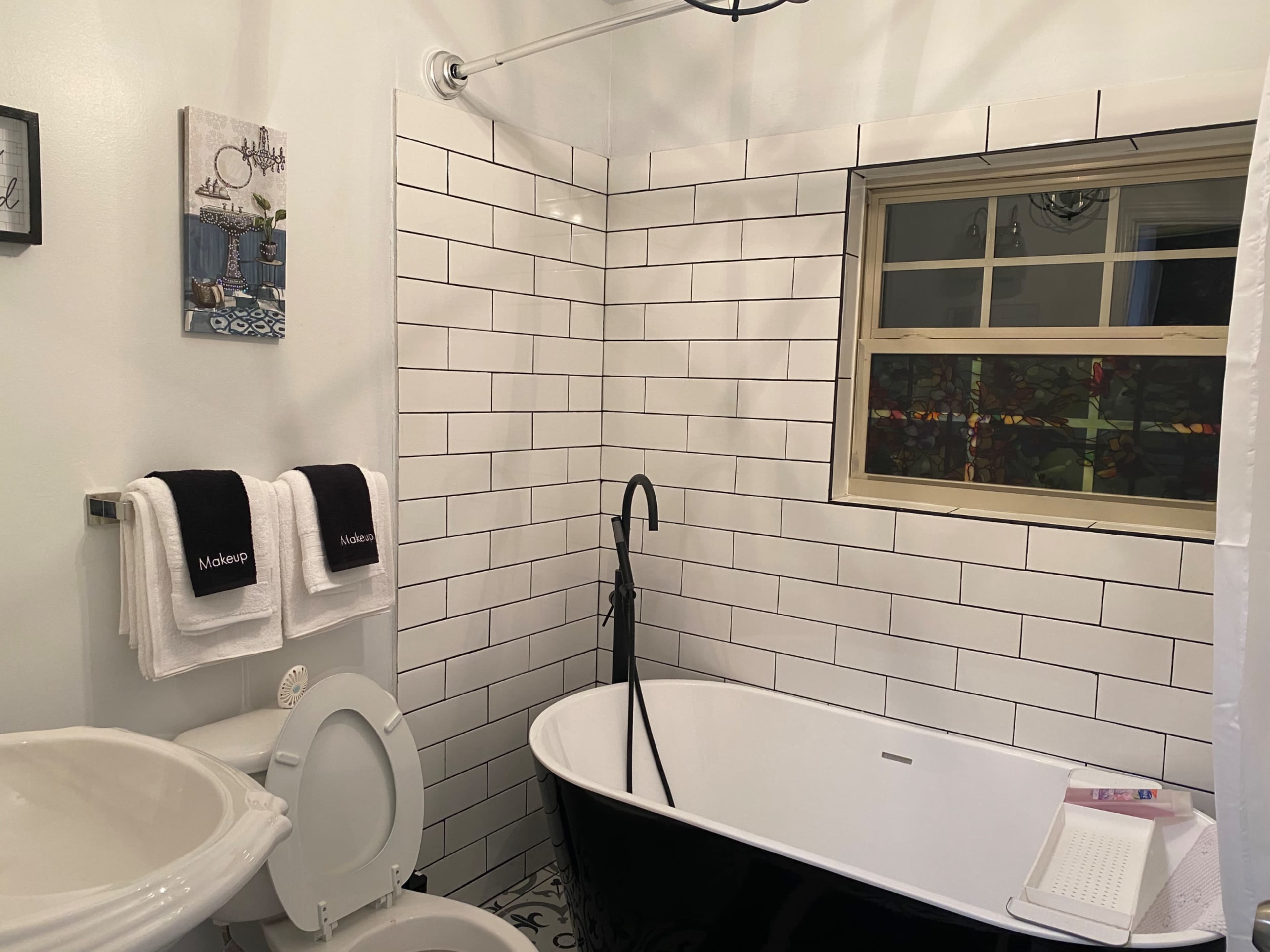 A modern bathroom featuring a black and white color scheme with a freestanding tub, a toilet, and tiled walls.