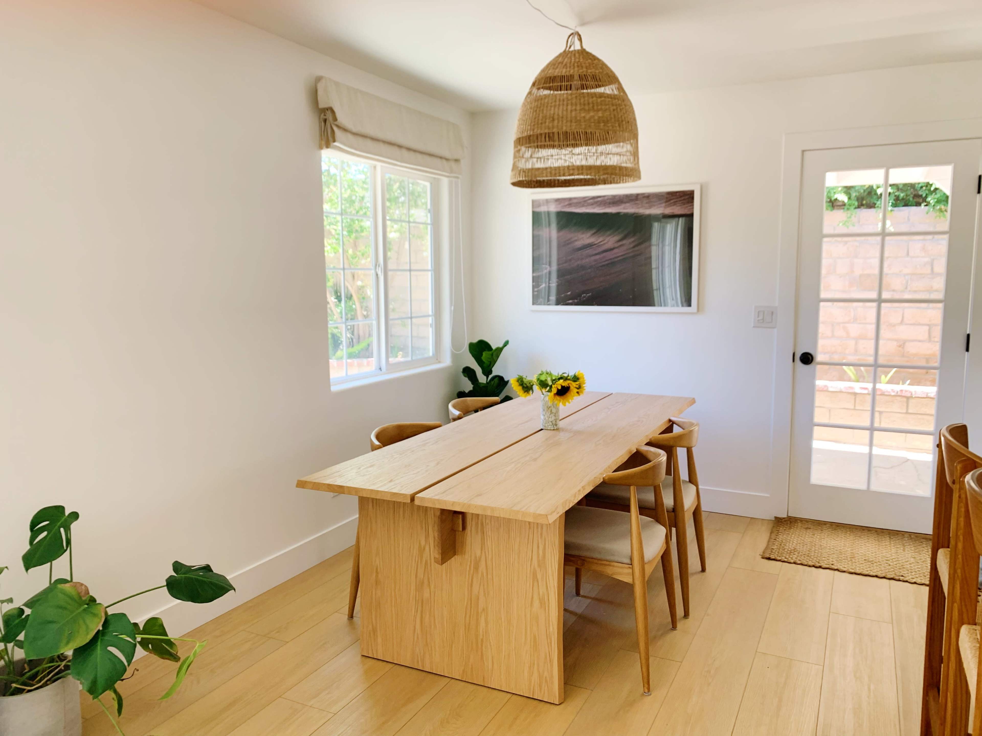 A well-lit dining area features a wooden table with sunflowers, surrounded by chairs, and a large window letting in natural light.