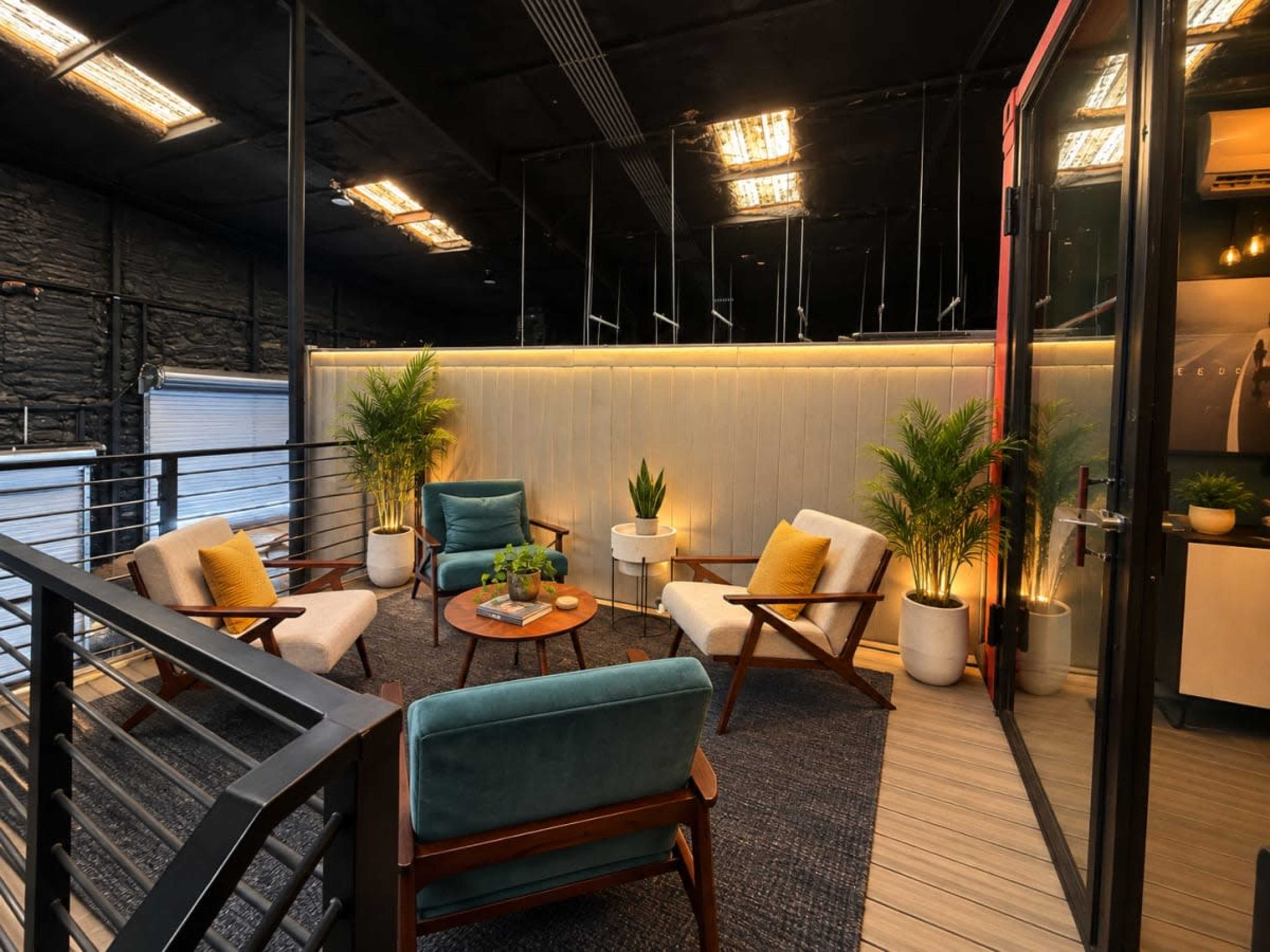 The image shows a modern lounge area featuring four chairs, a round table, and plants, situated in a well-lit space with a sleek design.