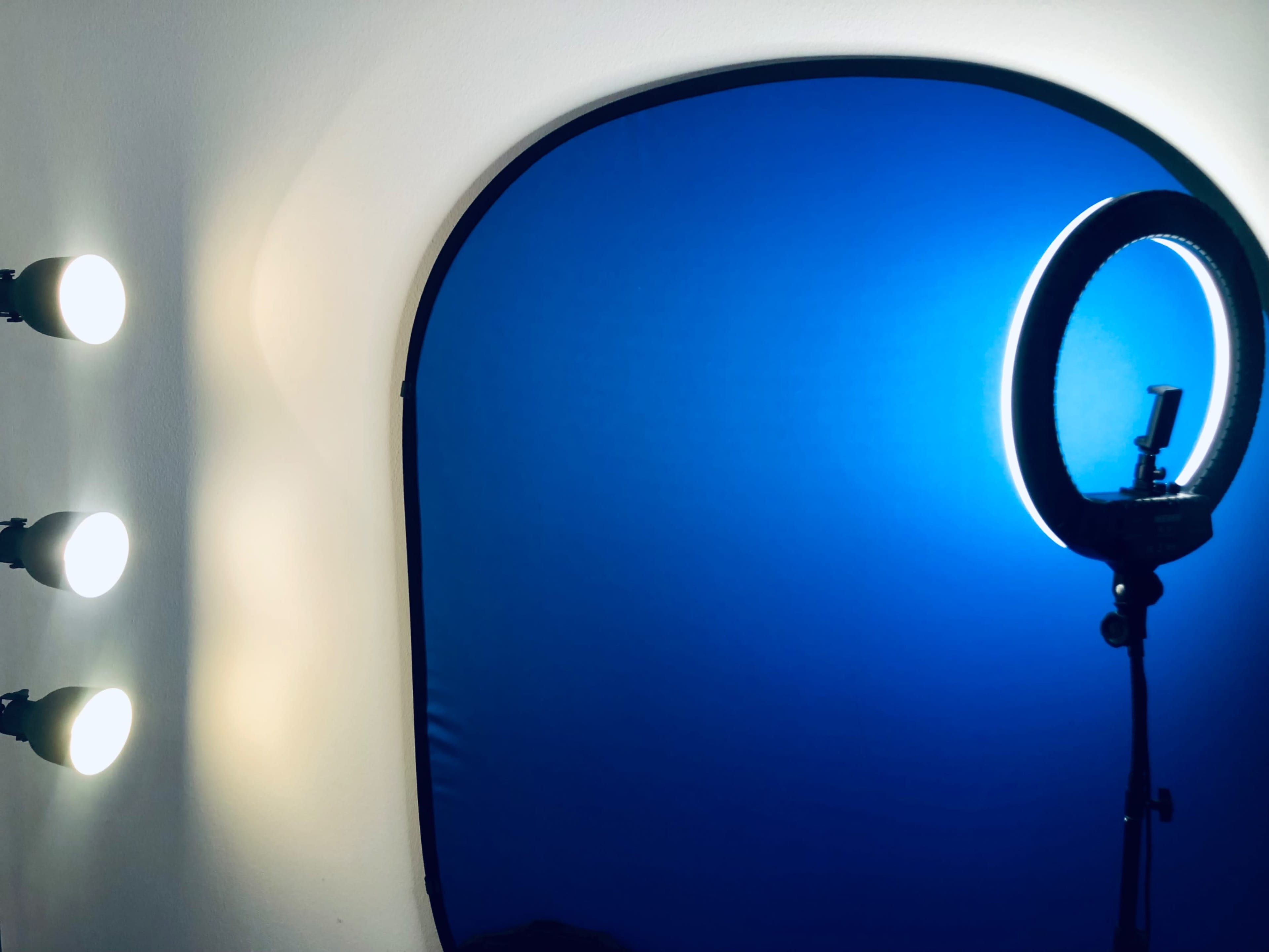 Three light fixtures mounted on a wall beside a circular light ring set against a blue backdrop.