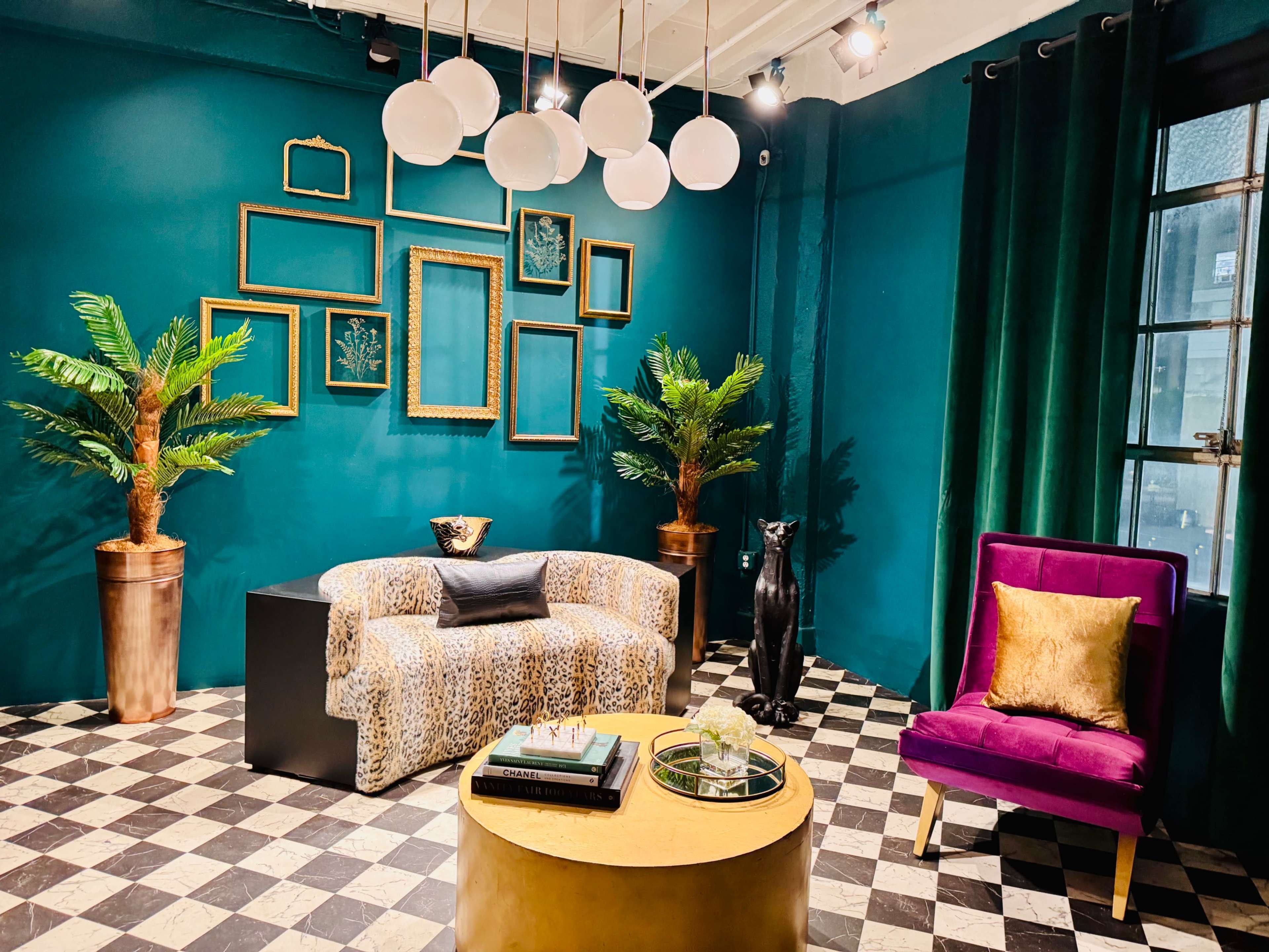 The image shows a stylish interior with a teal wall, a leopard-print sofa, a purple armchair, decorative plants, and framed art arranged on the wall.