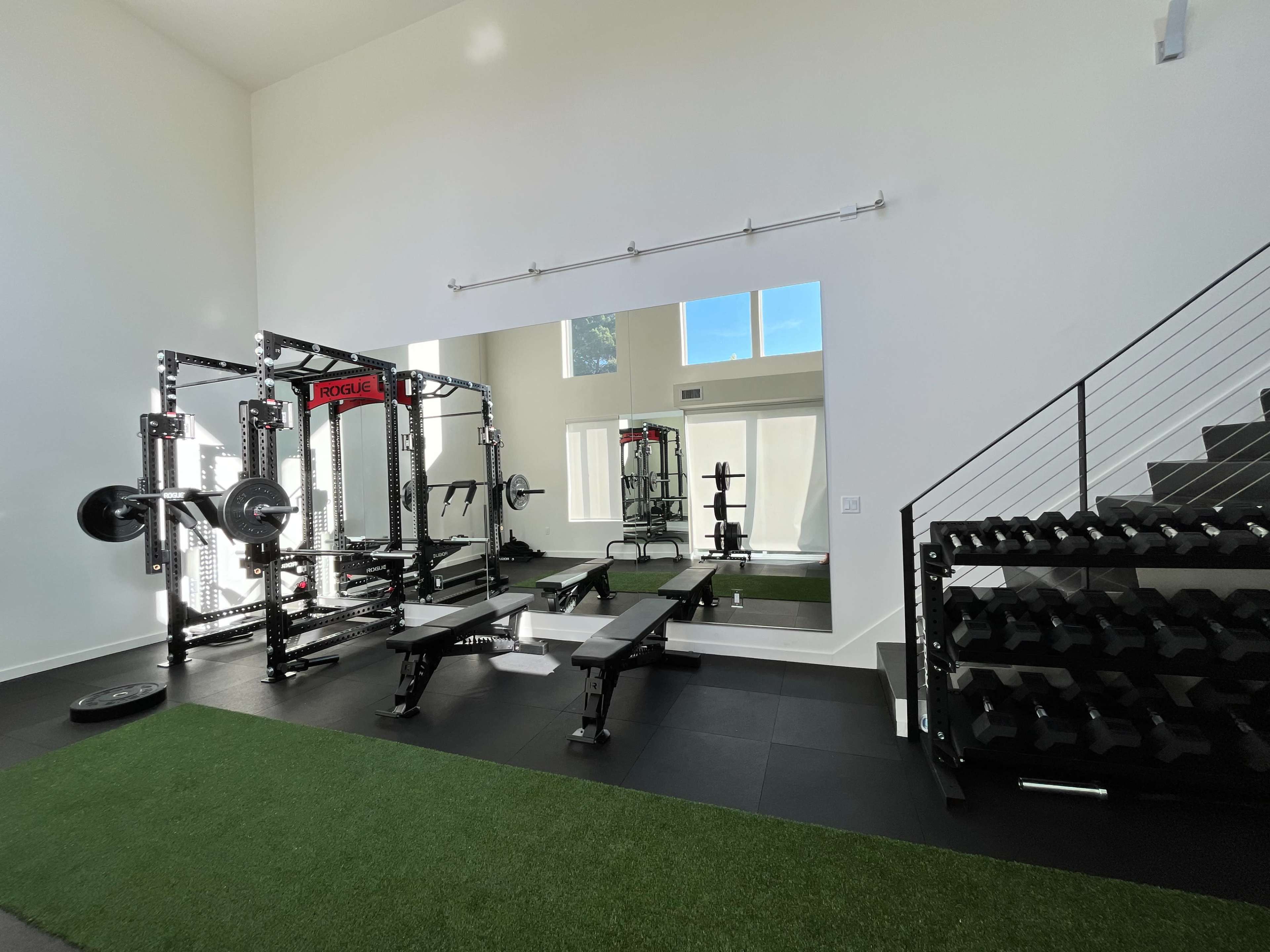 A well-equipped home gym featuring weightlifting equipment, benches, and a mirrored wall.
